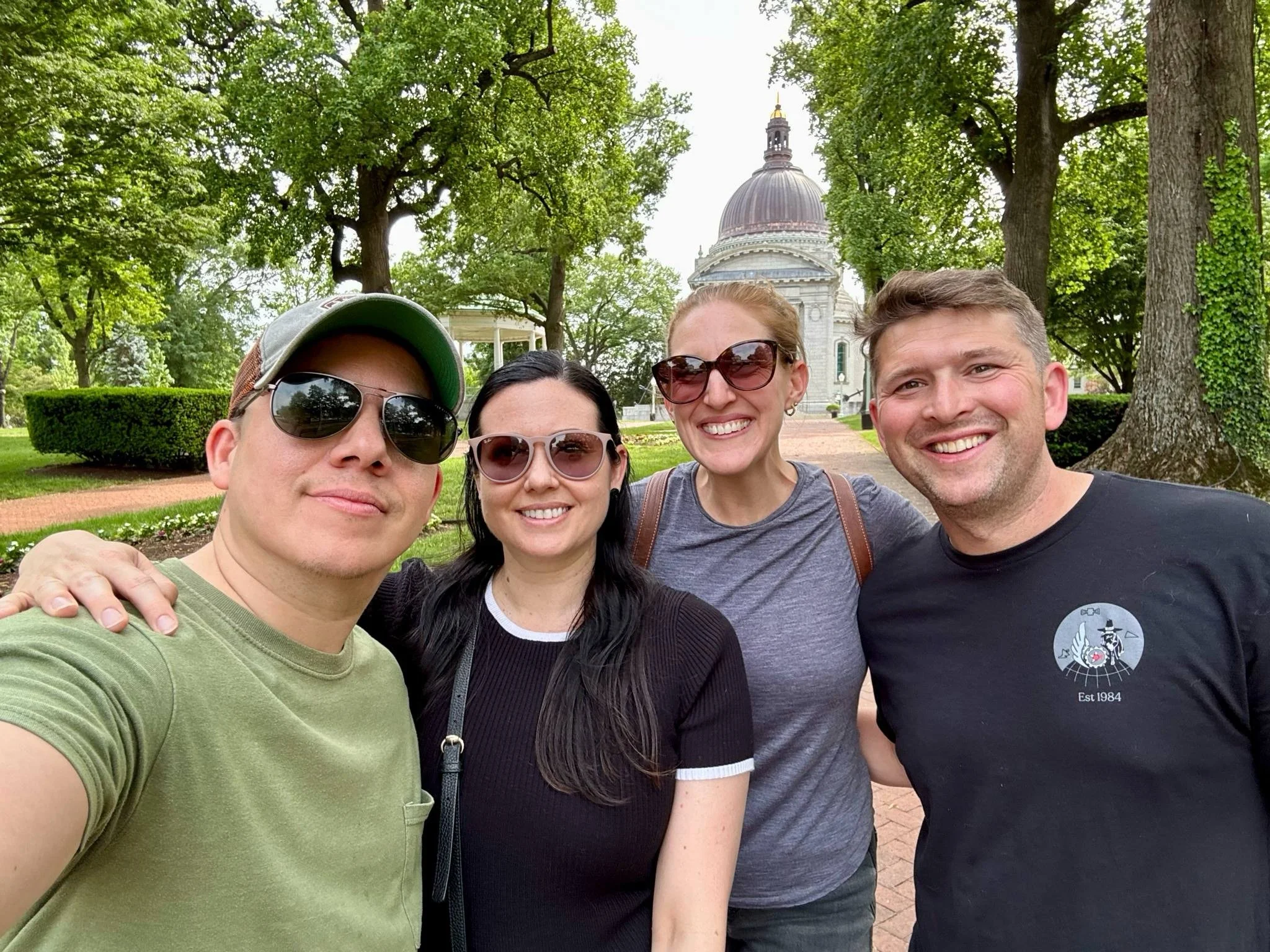 A group of friends posing together in a tree-lined park in Annapolis, Maryland, with the Maryland State House visible behind them. The photo captures a relaxed moment during a visit while traveling on the U.S. East Coast.