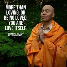 A person dressed in orange robes with hands in a prayer position, standing outdoors in a green, natural setting, with a quote by Spanda Makt about self-love.
