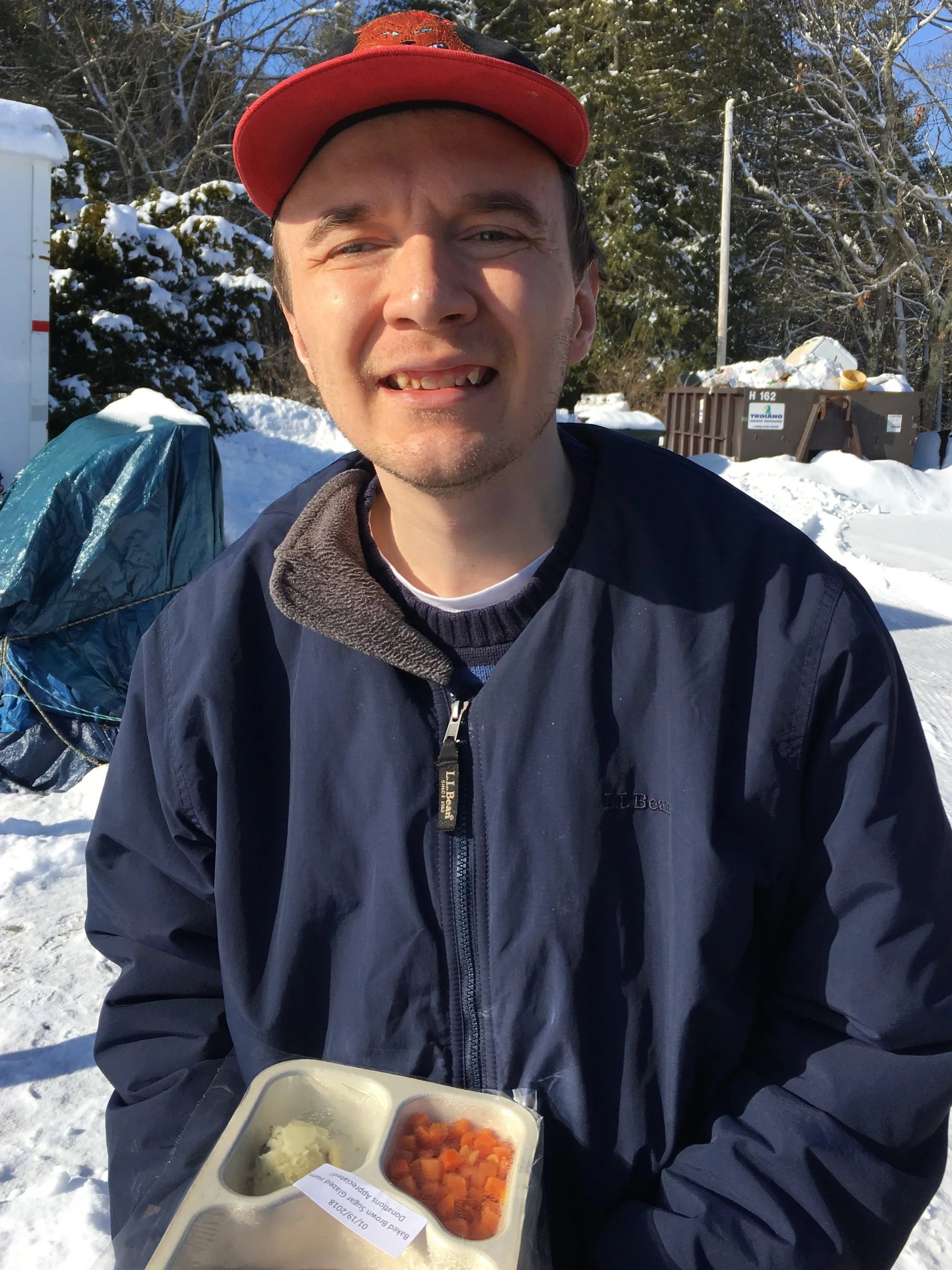 An Independence Association client carries a packaged meal -- complete with flatware -- across a snowy yard to an elderly person's residence. Our clients volunteer weekly to deliver Meals on Wheels.