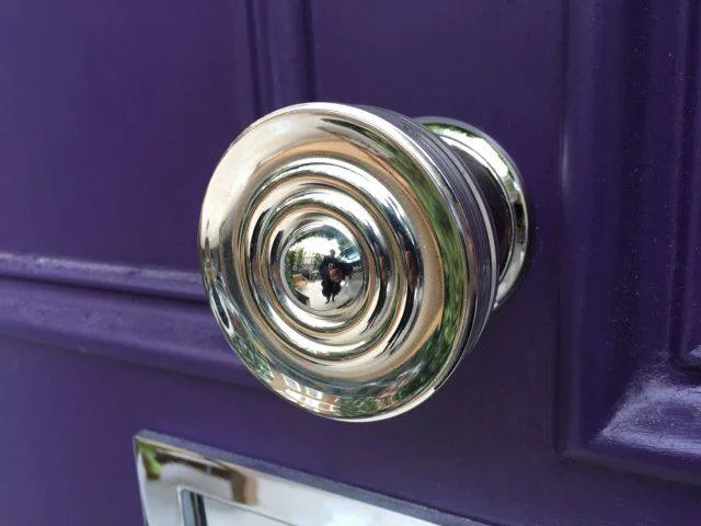 A purple front door with gleaming chrome hardware. Purple chosen to work with the beautiful wisteria that covers the building walls.
