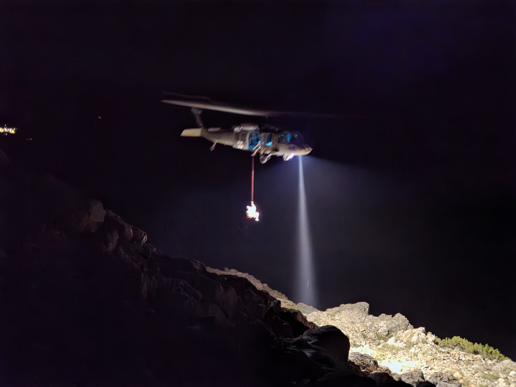 Helicopter with a lowered medic over the dark mountain
