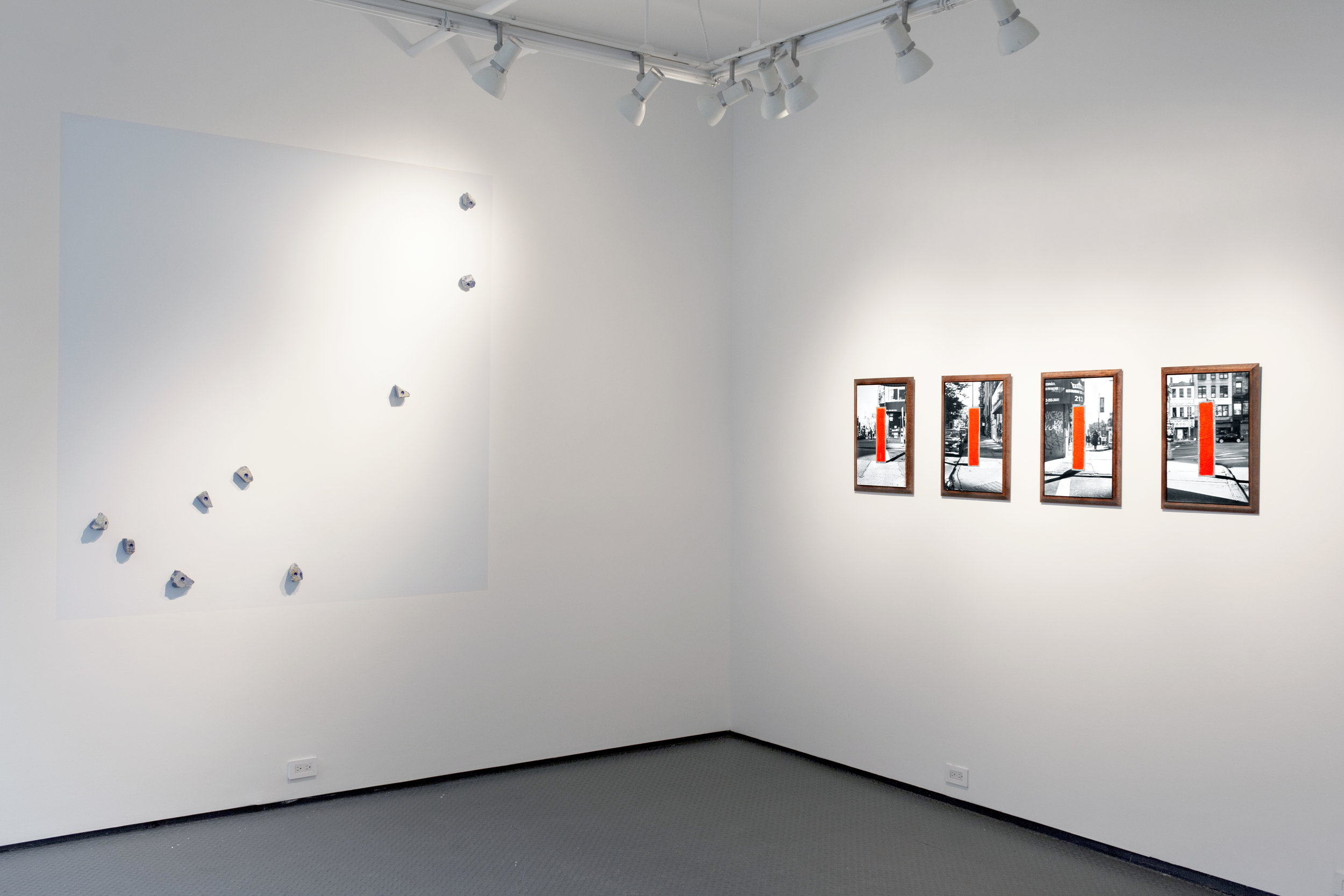 Inside the gallery, Alarm Amann consists of four photographs of the fire alarm, painted with the same red and framed with the same molding that ornaments the alarm. On the west wall, an installation consisting of nine lapis lazuli rough rocks directly screwed in the wall remasters Constellation of Street Corners, a piece previously shown on the same gallery wall in July 2014 when the artist documented the location of nine Blue Puddle interventions on a large scale downtown map.