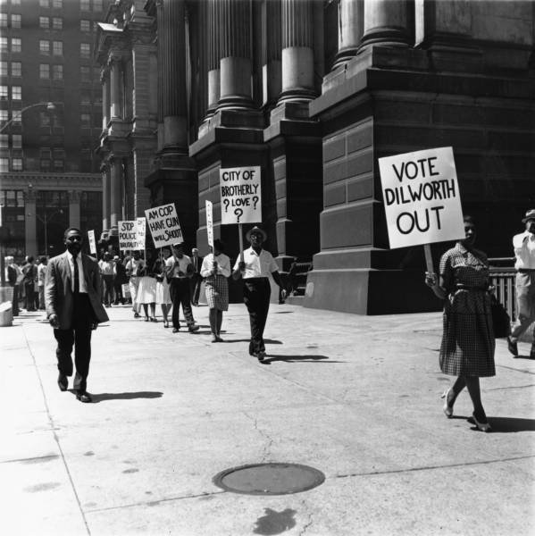   A protest against police brutality, 1960. Protestors circle City Hall on foot following the funeral service for Ella Lucy Jones and Louise Jones. Some signs read “Vote Dilworth Out,” “City of brotherly love?” “Am cop, have gun, will shoot,” and “St
