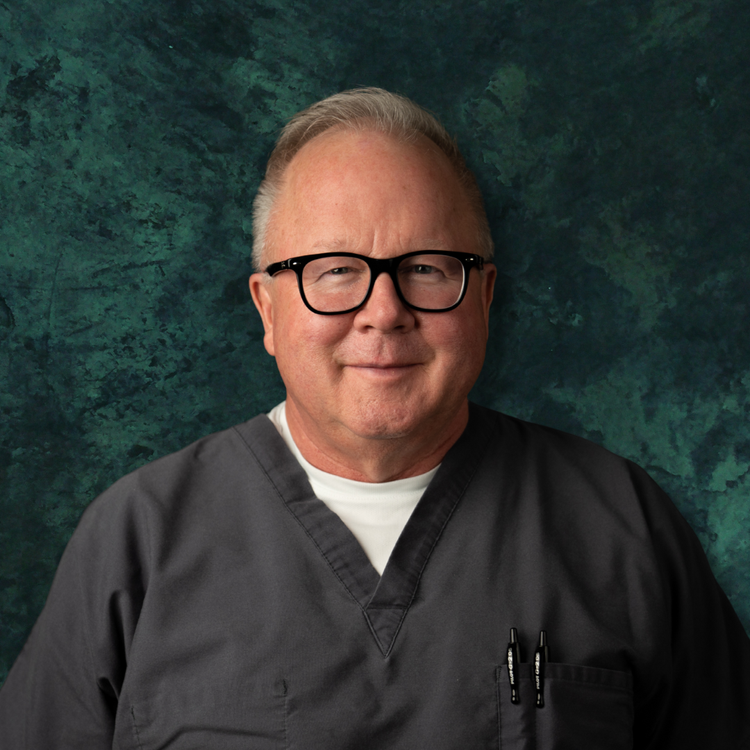 Dr. Dan Purser in clinic scrubs against a dark teal backdrop