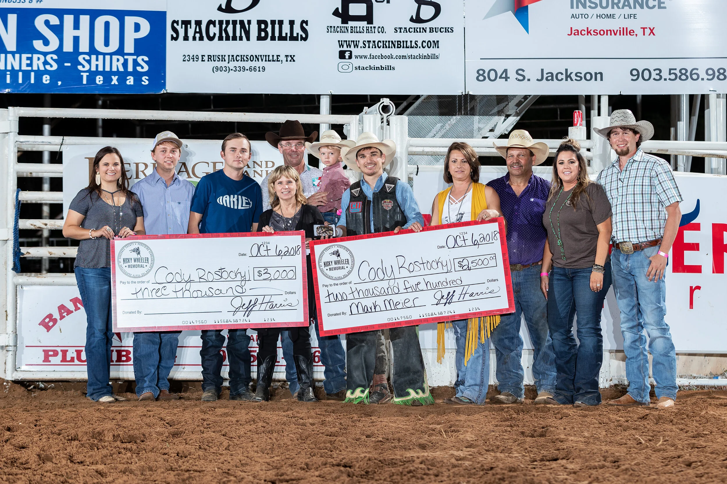 Tuff Hedeman presents the check to last years champ Cody Rostockyj. The Nicky Wheeler Memorial Bull Riding serves as the primary fundraiser for the youth of Cherokee County. Co-Producers, Jeff Harris and Family, Haley and Brian Beasley with the Nicky Wheeler family, and Tuff Hedeman and son. Photo by Todd Brewer.