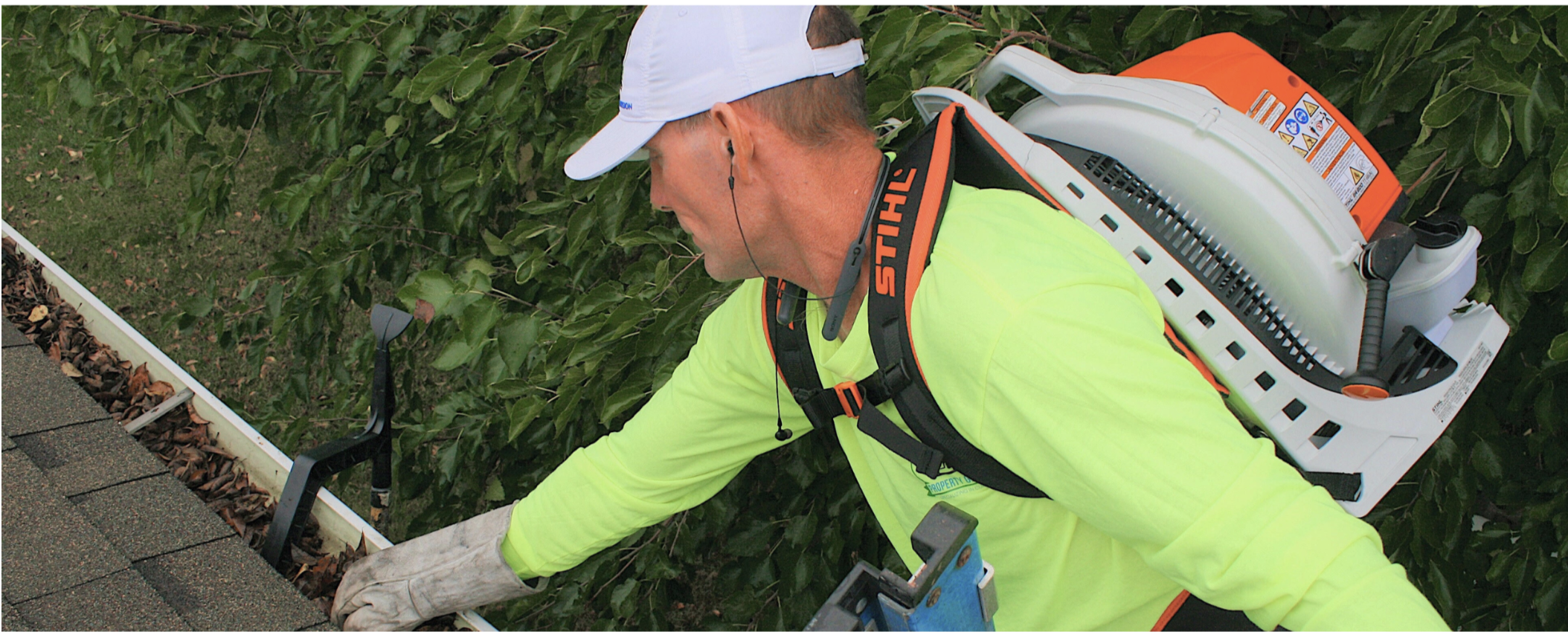 Man on ladder cleaning leaves out of gutter