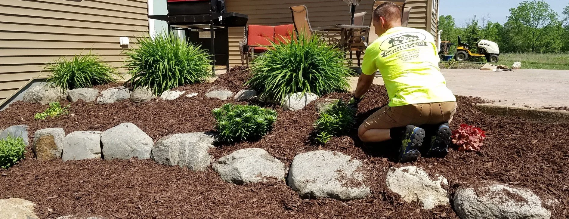 man fixing landscaping by cleaning up mulch and adding shrubs