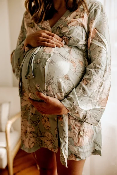 pregnant woman holding her baby bump dressed in a floral maternity robe