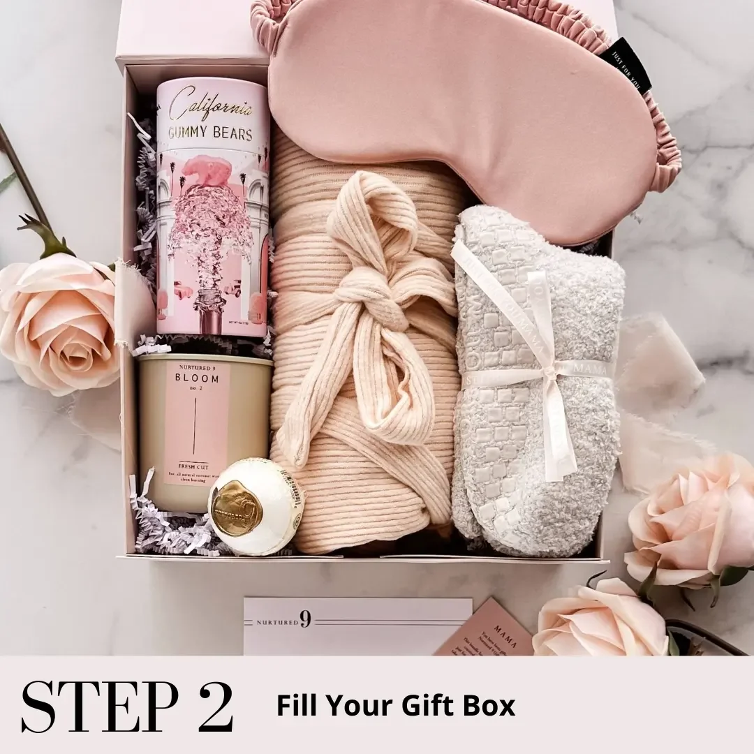 an open pregnancy gift box with gift items inside including a satin sleep mask, candle, bath bomb, maternity robe and fluffy socks