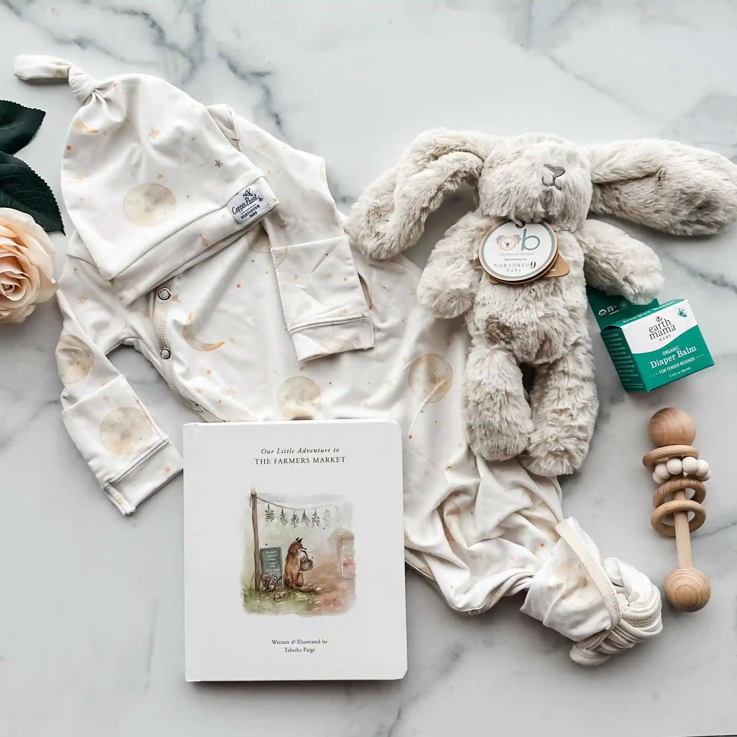 newborn gown, newborn hat, board book, diaper balm, rattle, and a bunny stuffy on a marble background