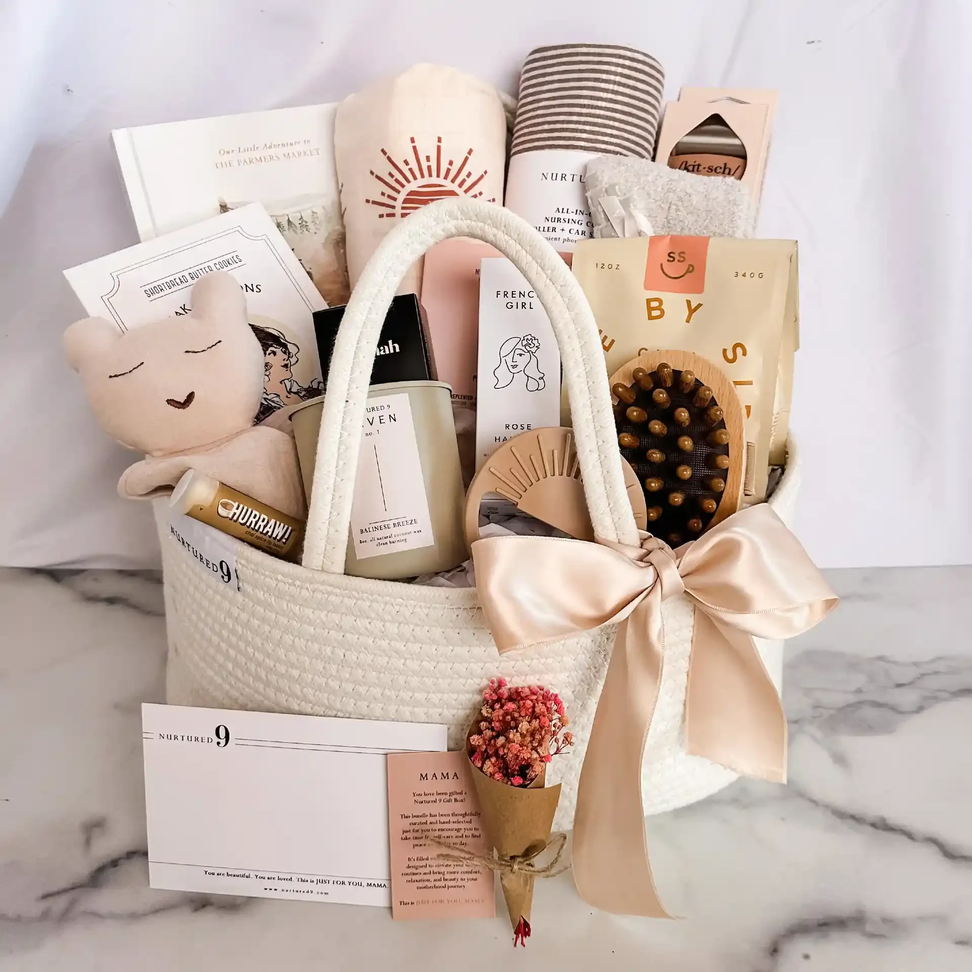 new mom gift basket with gift items including lovey, swaddle, nursing cover, teether, scalp brush, chai tea mix, ice roller, hospital socks