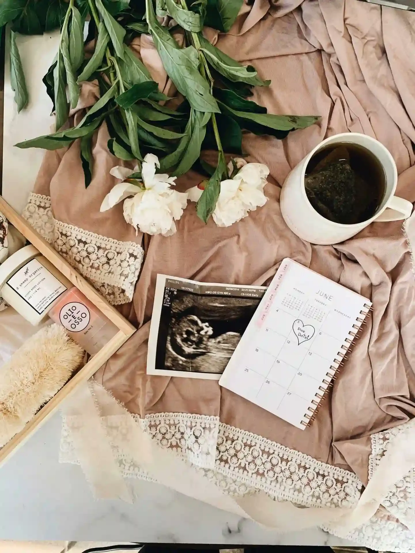 pregnancy due date on calendar, ultrasound, mug with tea, maternity robe, and flowers