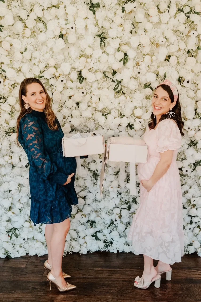 two pregnant moms holding a gift box and their baby bump