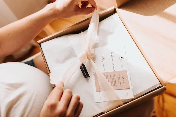 pregnant woman untieing ribbon on an open gift box with tissue paper
