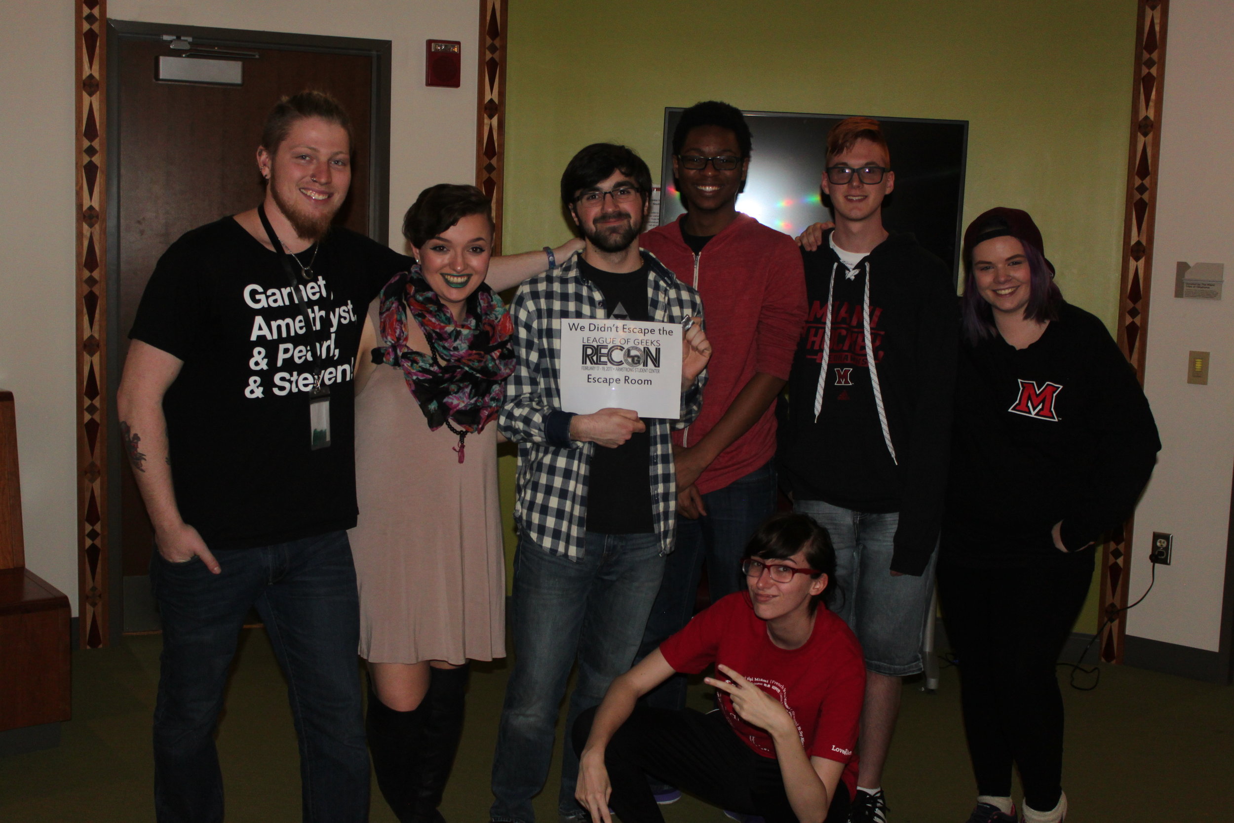 A group of people, one in the middle holding a piece of paper that says "we didn't escape the RECON escape room"