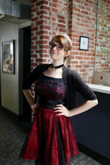  A white woman in glasses and tiara in front of a hallway that goes to brick  behind her and then a window. 