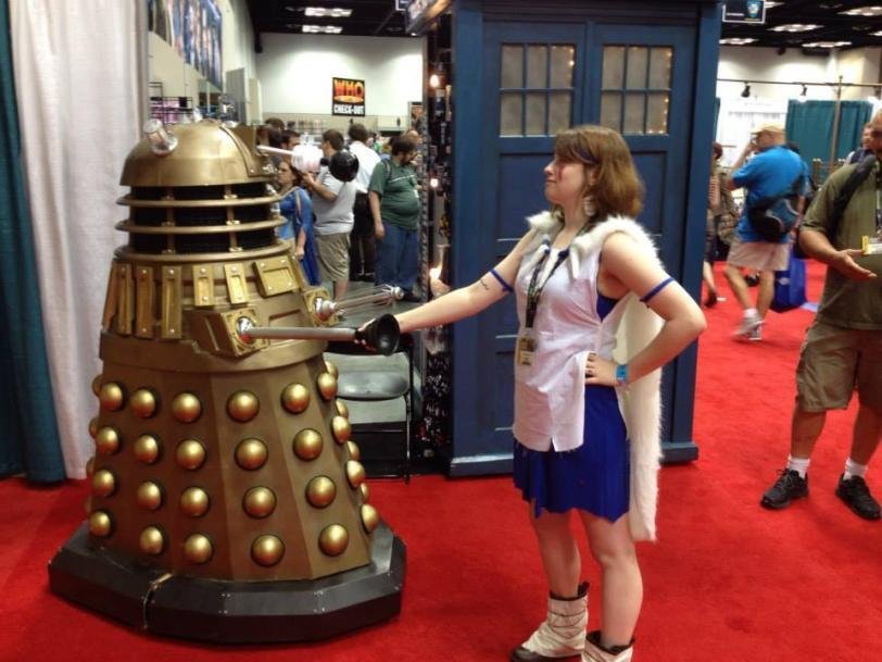  People at a con with the focus on a dalek greeting a white woman in glasses. 