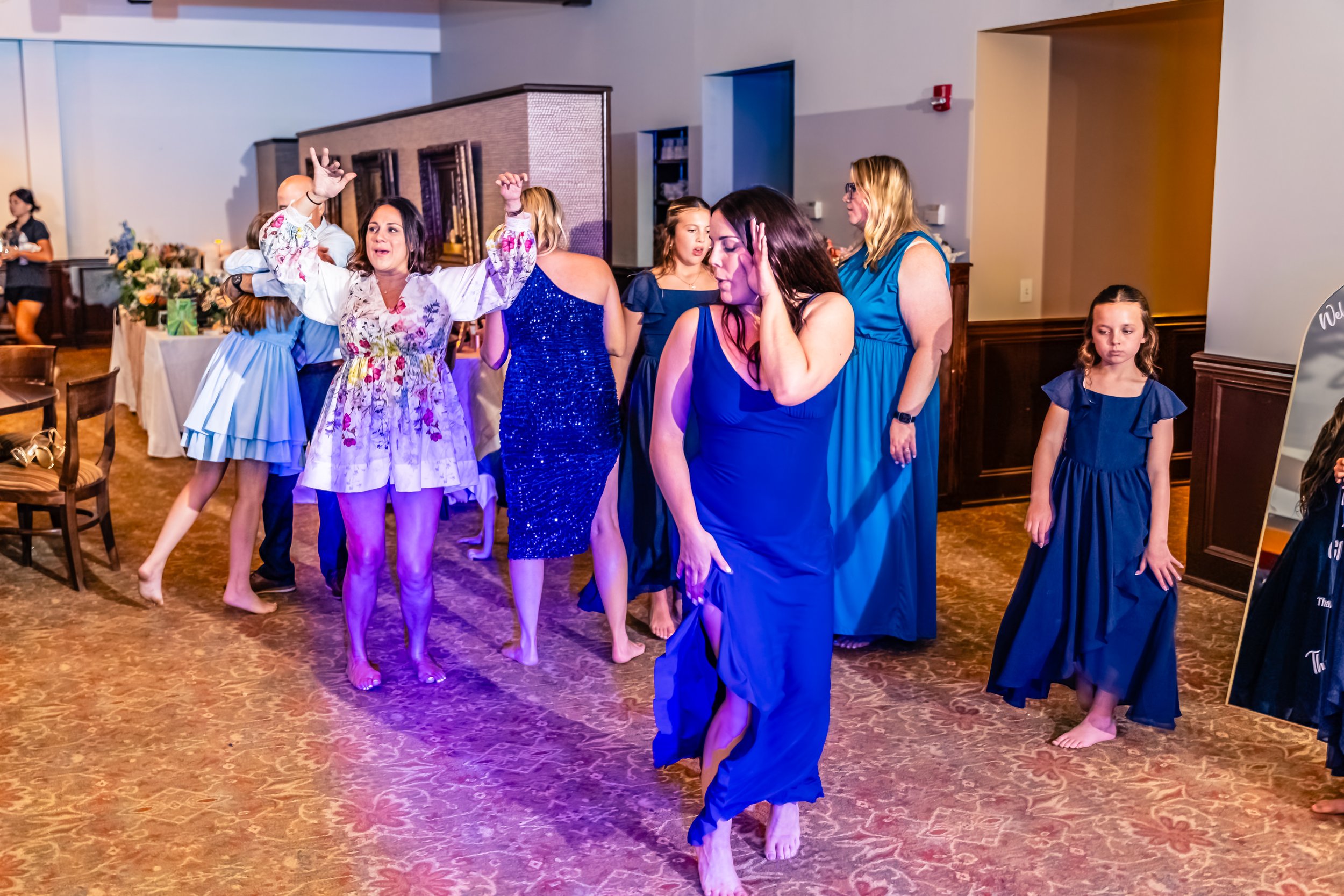People dancing and celebrating at a party in a banquet hall with blue dresses and colorful attire.