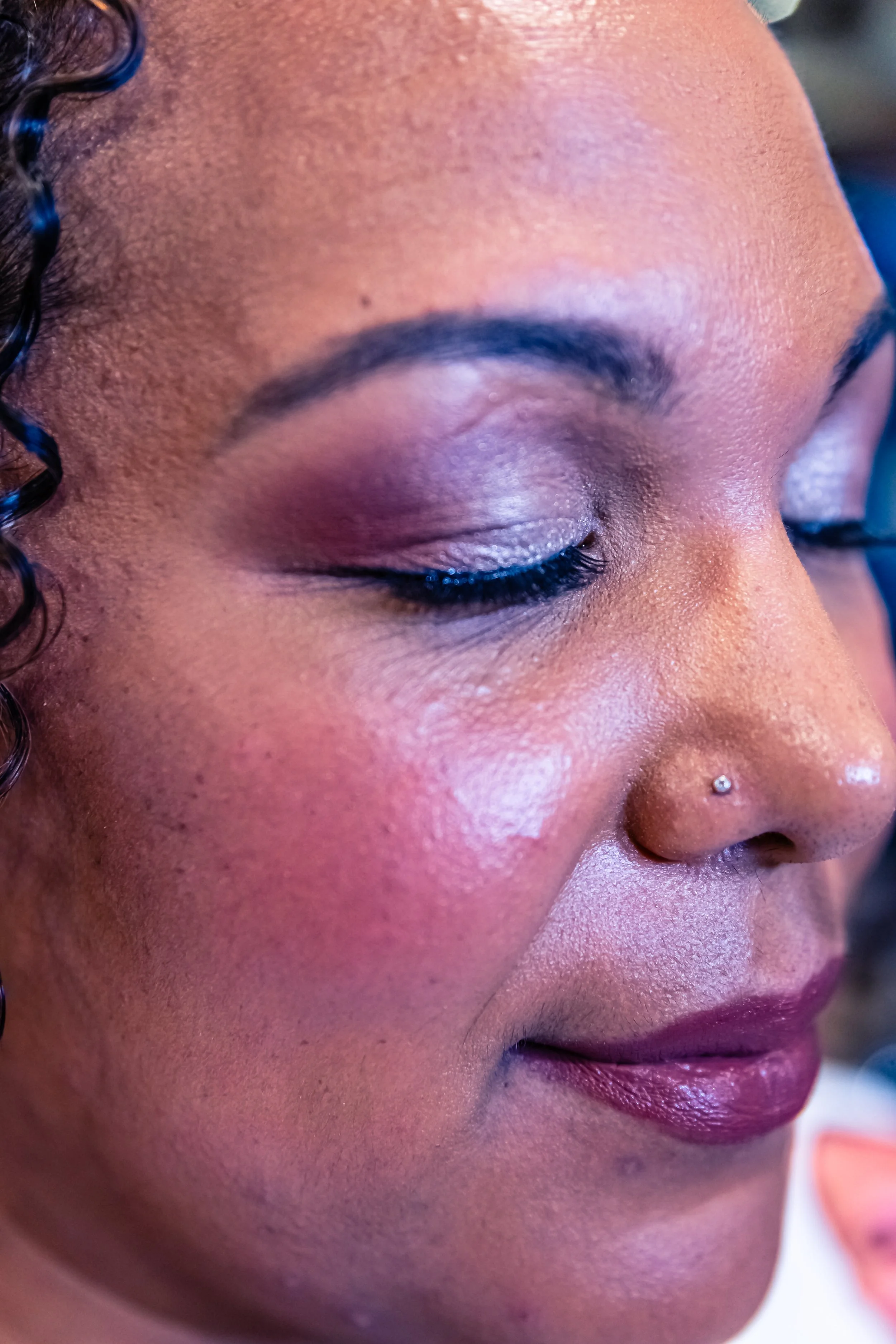 Close-up of a woman's face with makeup, closed eyes, and a small nose piercing.
