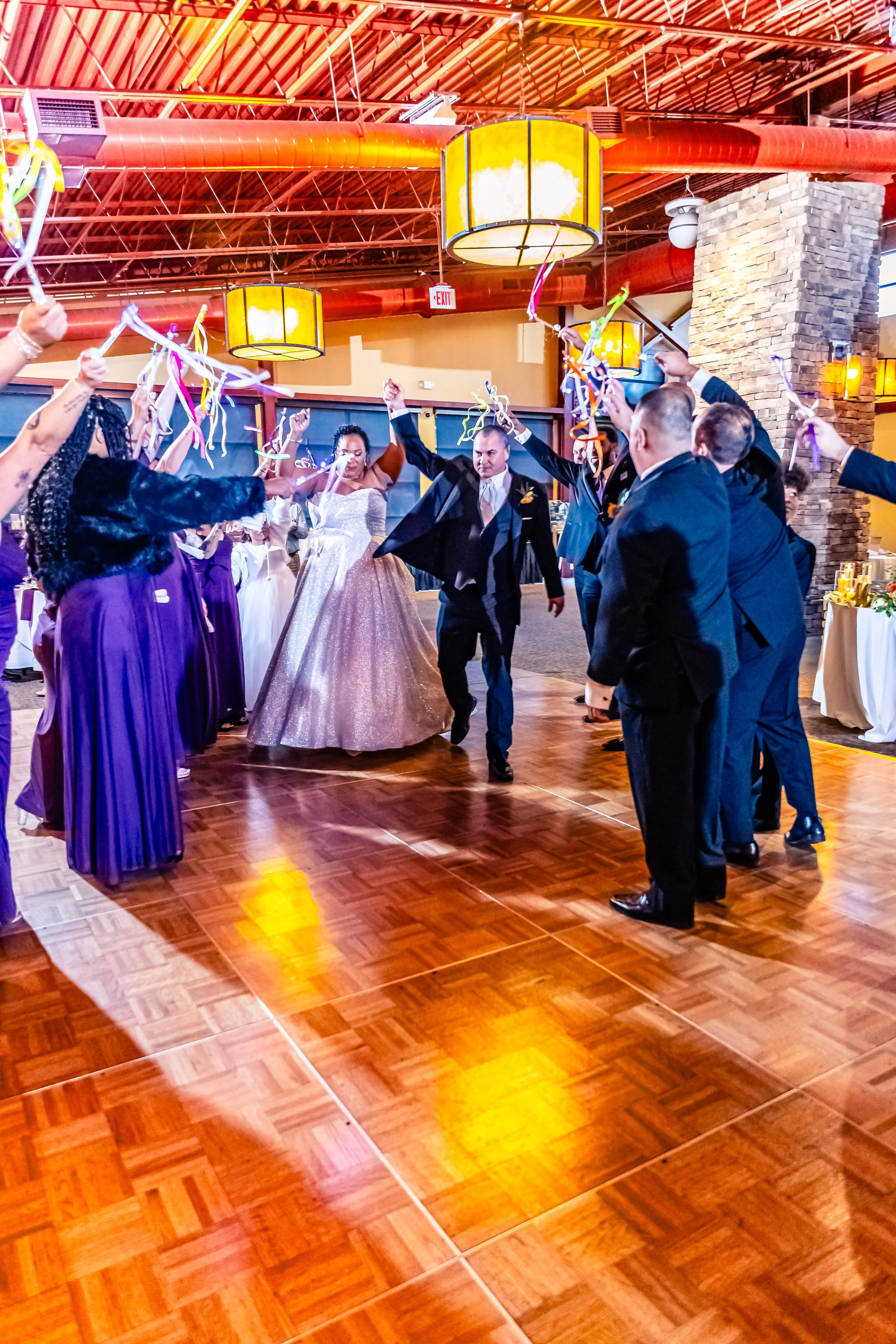 People dancing at a wedding reception under warm lighting, with some holding colorful streamers.