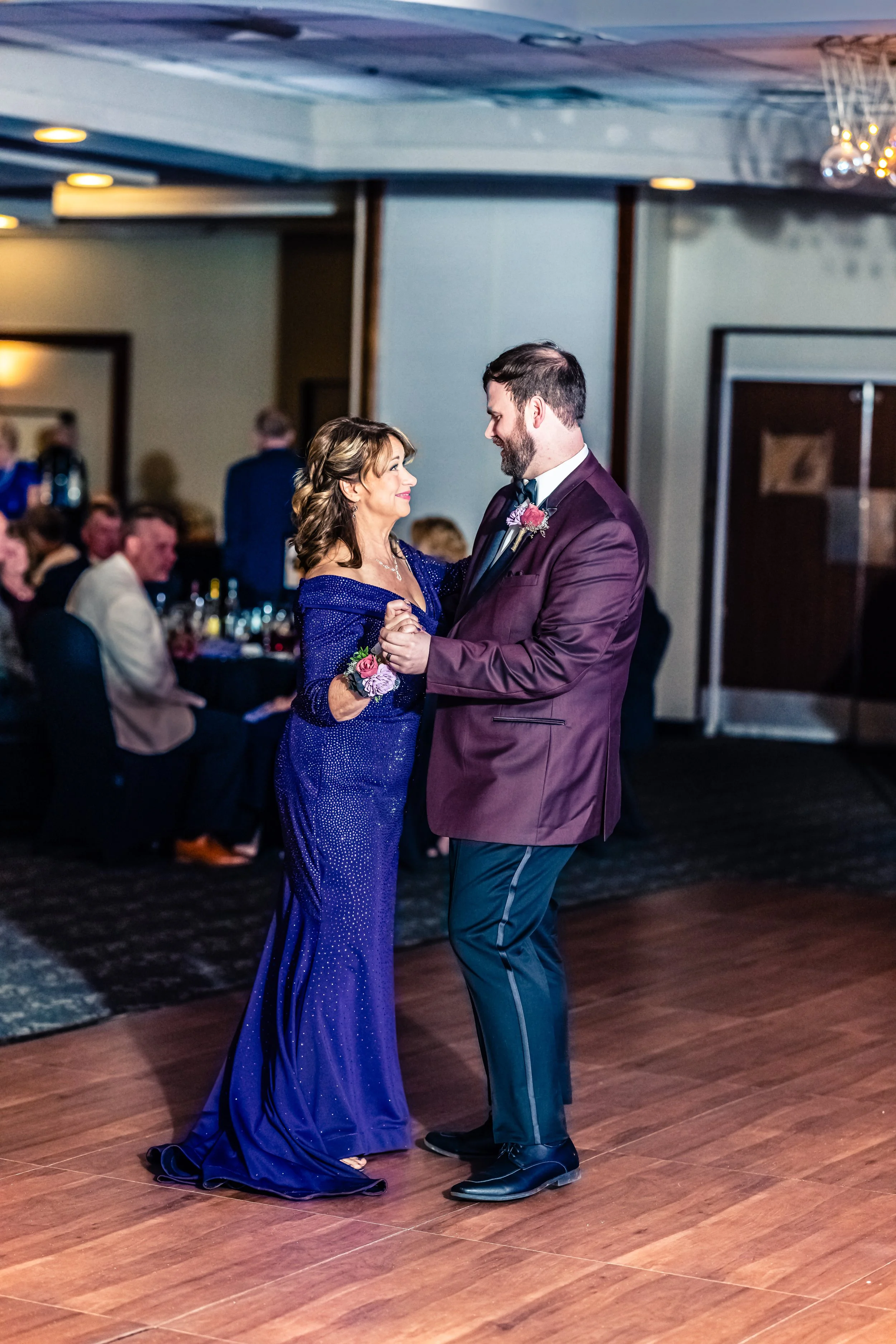 A woman in a formal blue gown dancing with a man in a maroon suit at a wedding reception.