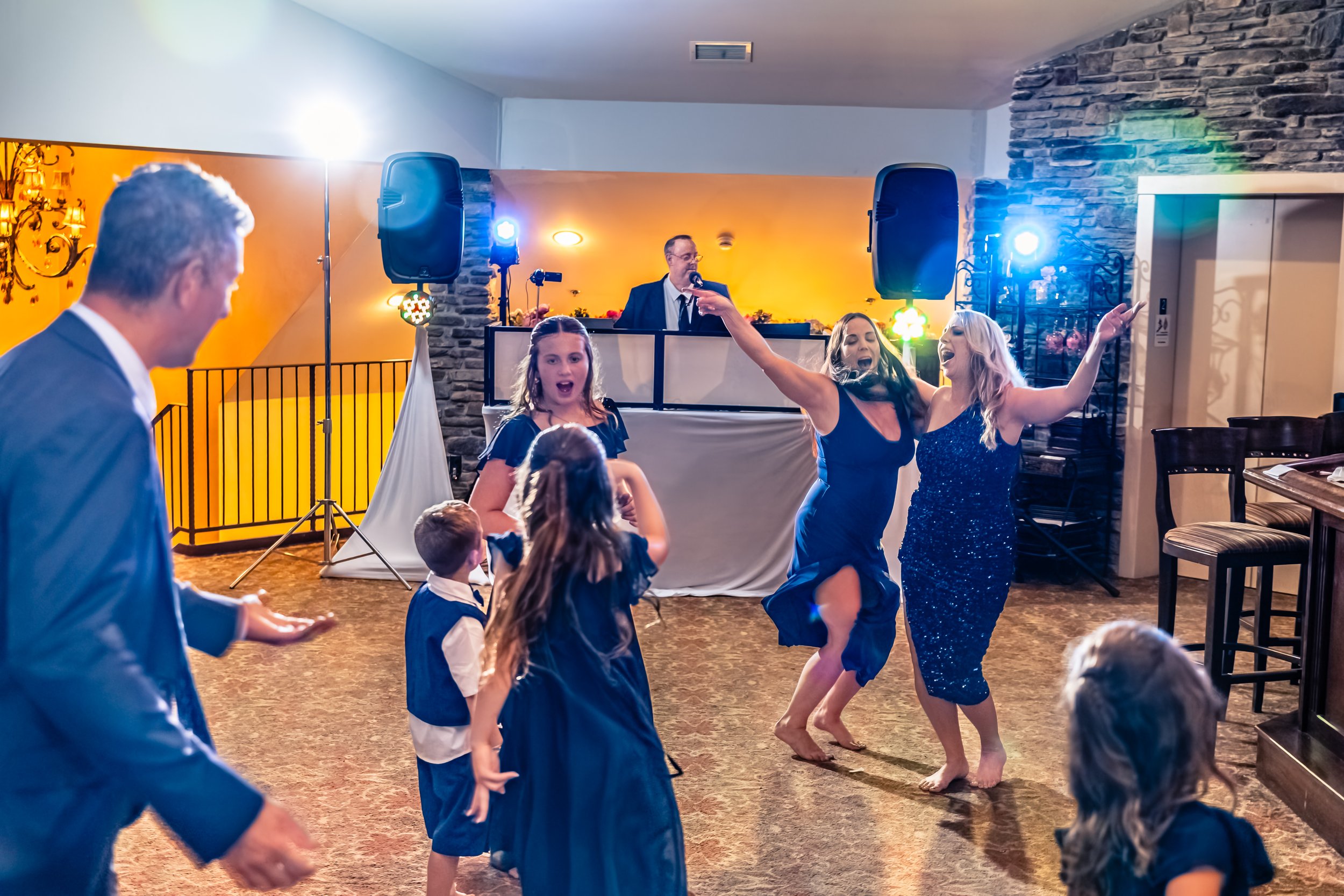 People dancing and singing at a celebration or party with a DJ in the background.