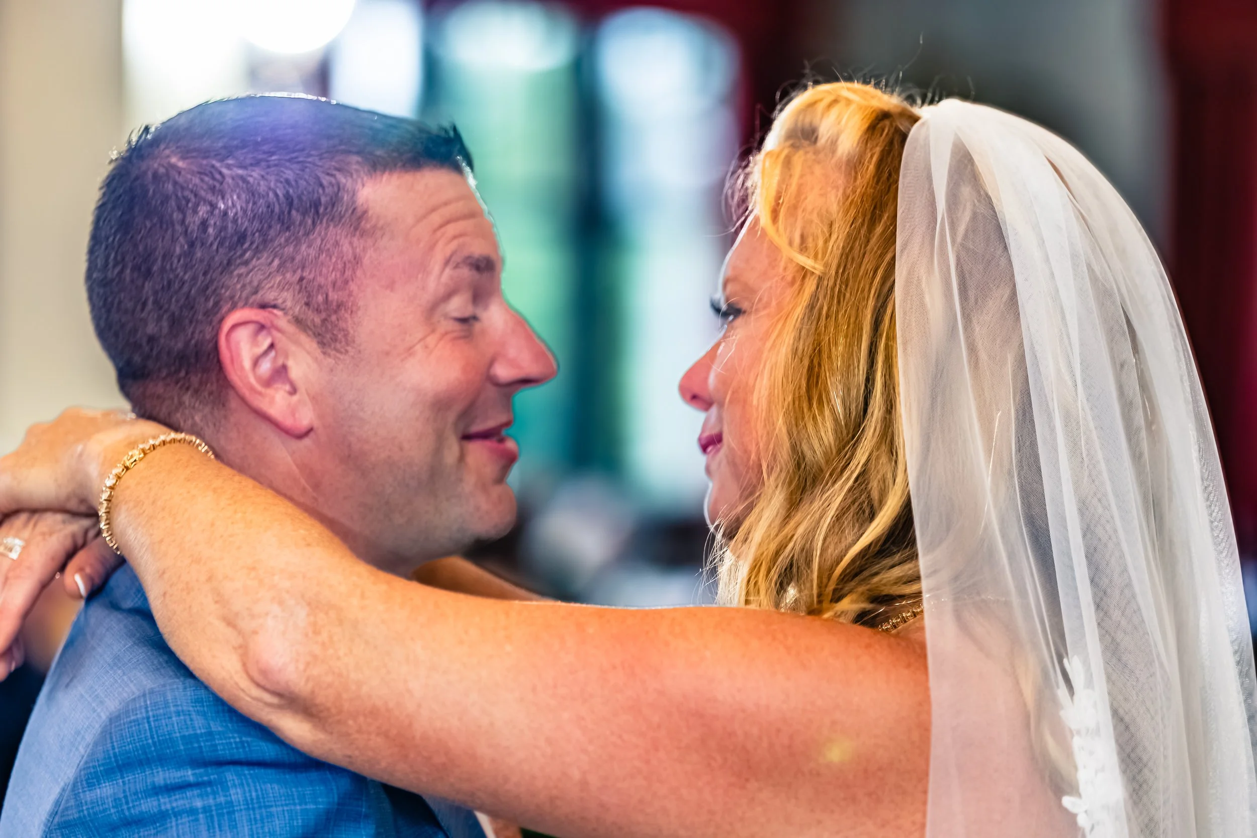 A bride and groom sharing a close, intimate moment, with the bride wearing a white veil and the groom in a blue suit, smiling and gazing into each other's eyes.