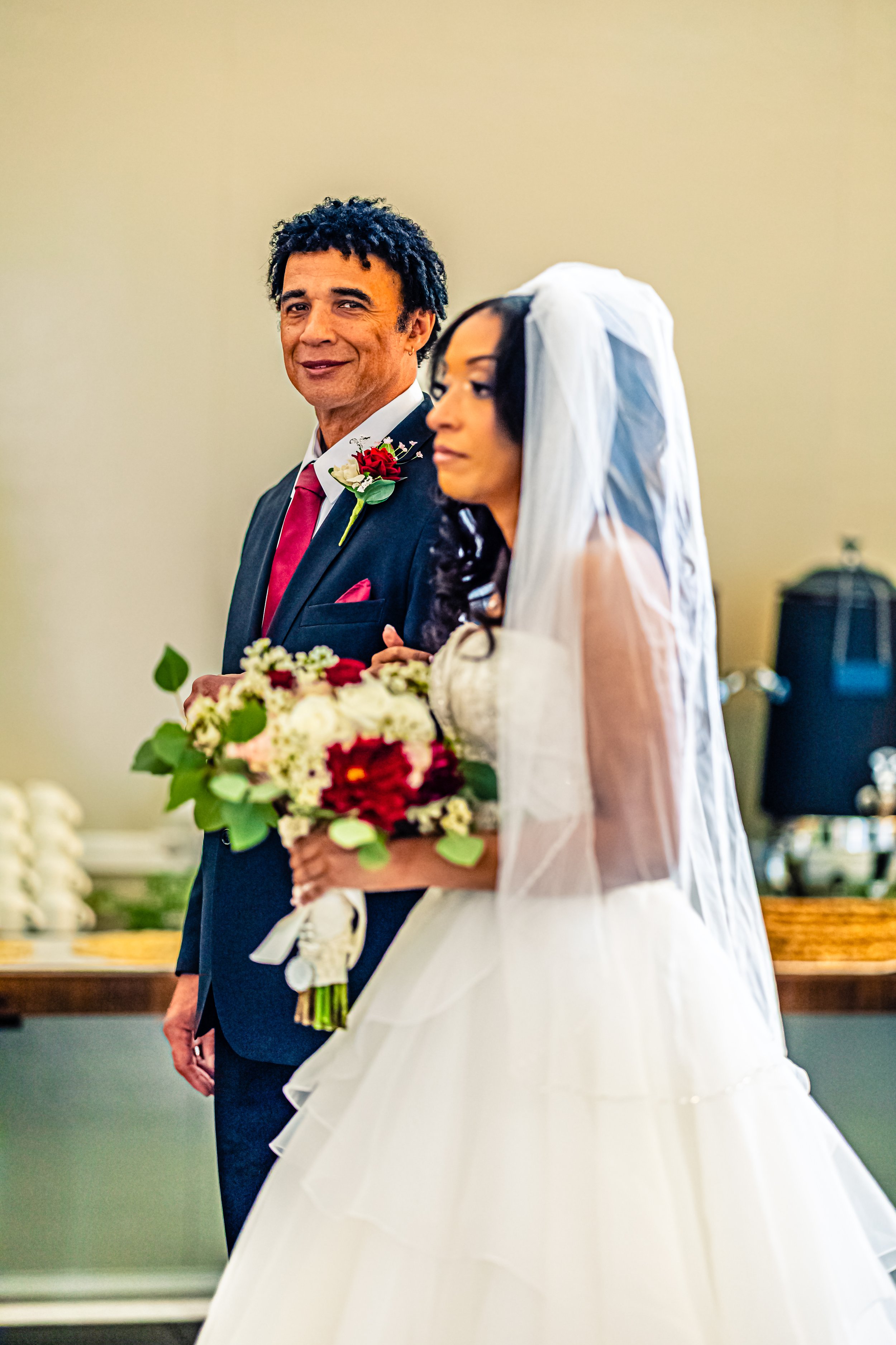 A groom and bride standing side by side during a wedding ceremony, with the groom smiling and the bride holding a bouquet of flowers.