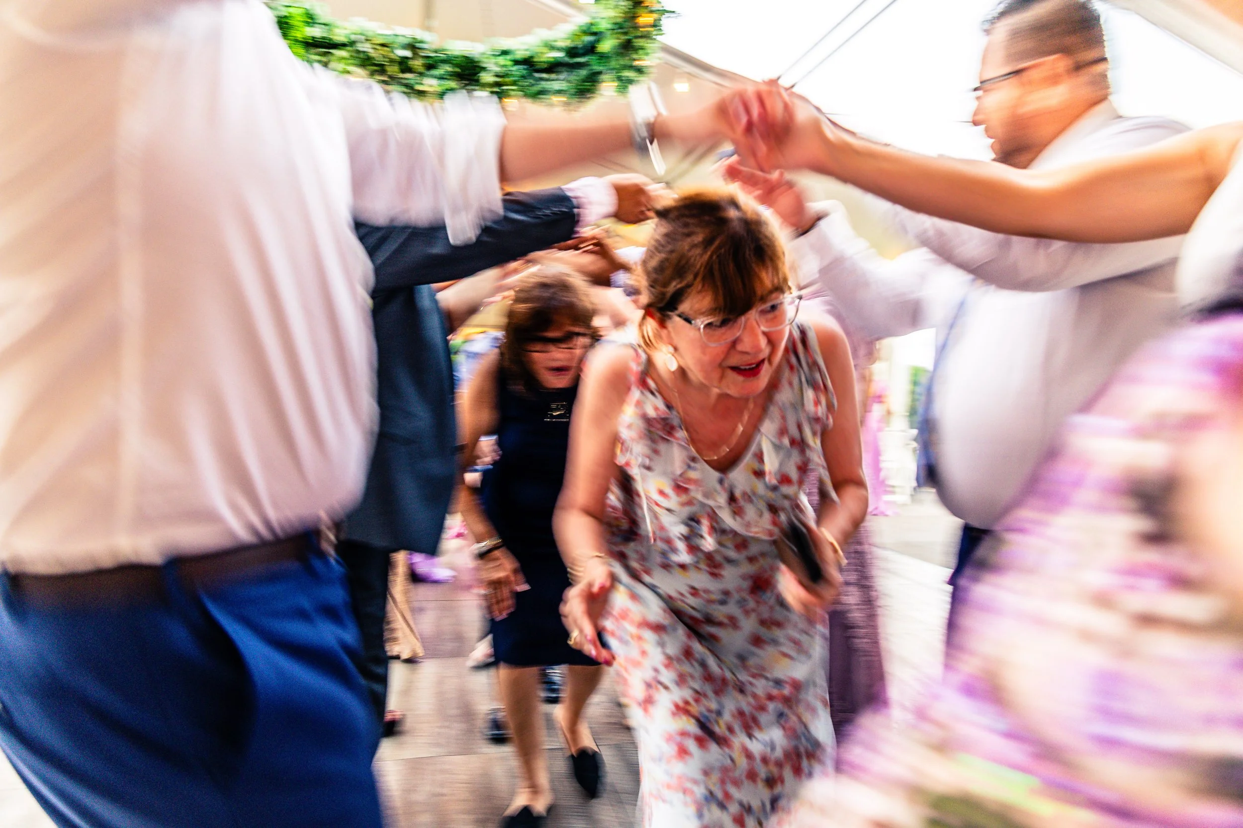 People dancing and playing during a celebration, with a woman in the center wearing glasses and a floral dress.