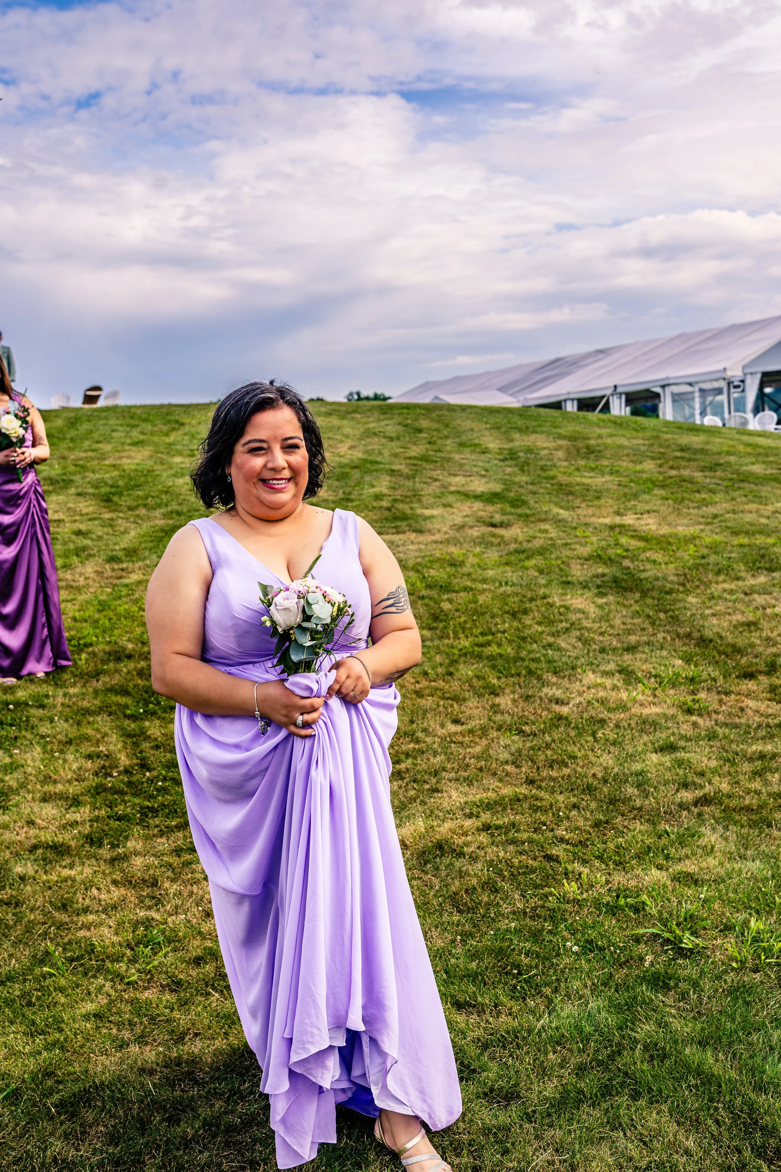 Woman in a lavender dress holding a bouquet of flowers outdoors at a wedding.