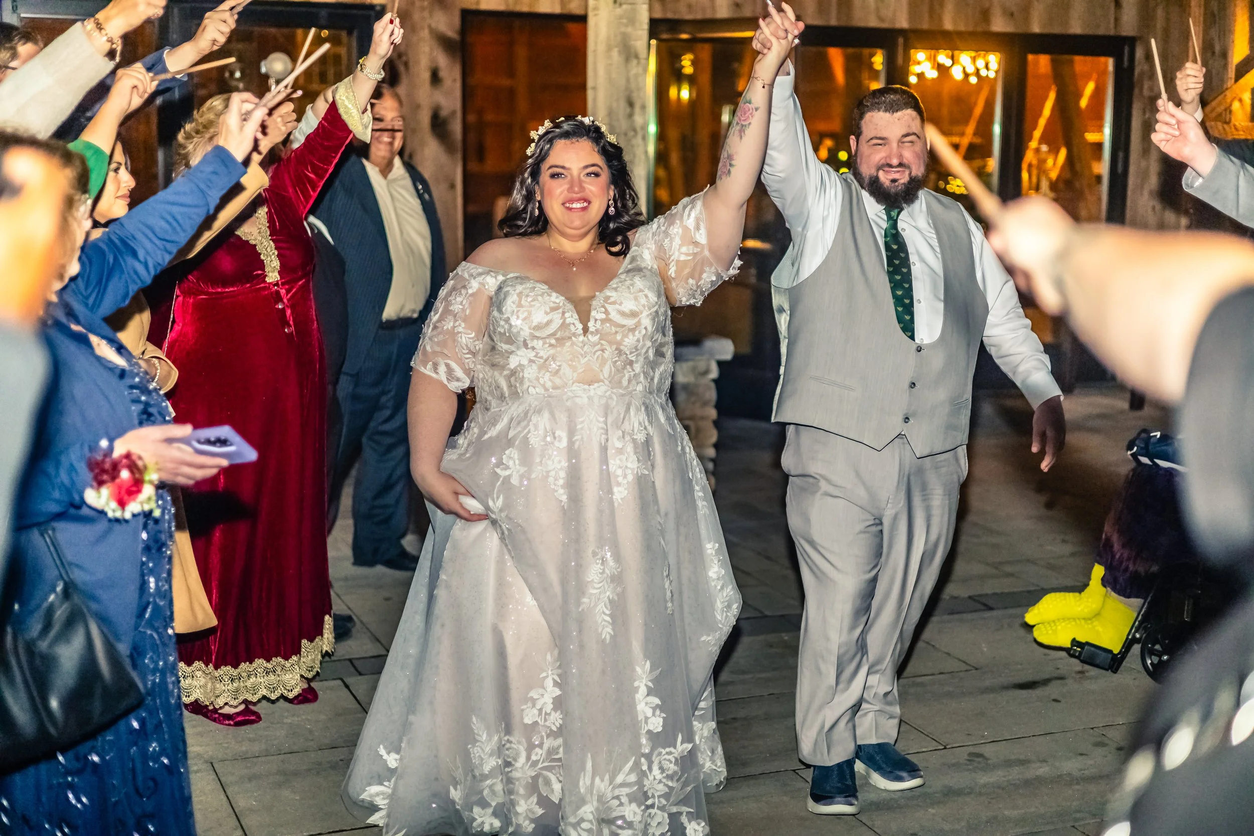Bride and groom holding hands up while walking through a celebration surrounded by guests holding sparklers inside a rustic venue.
