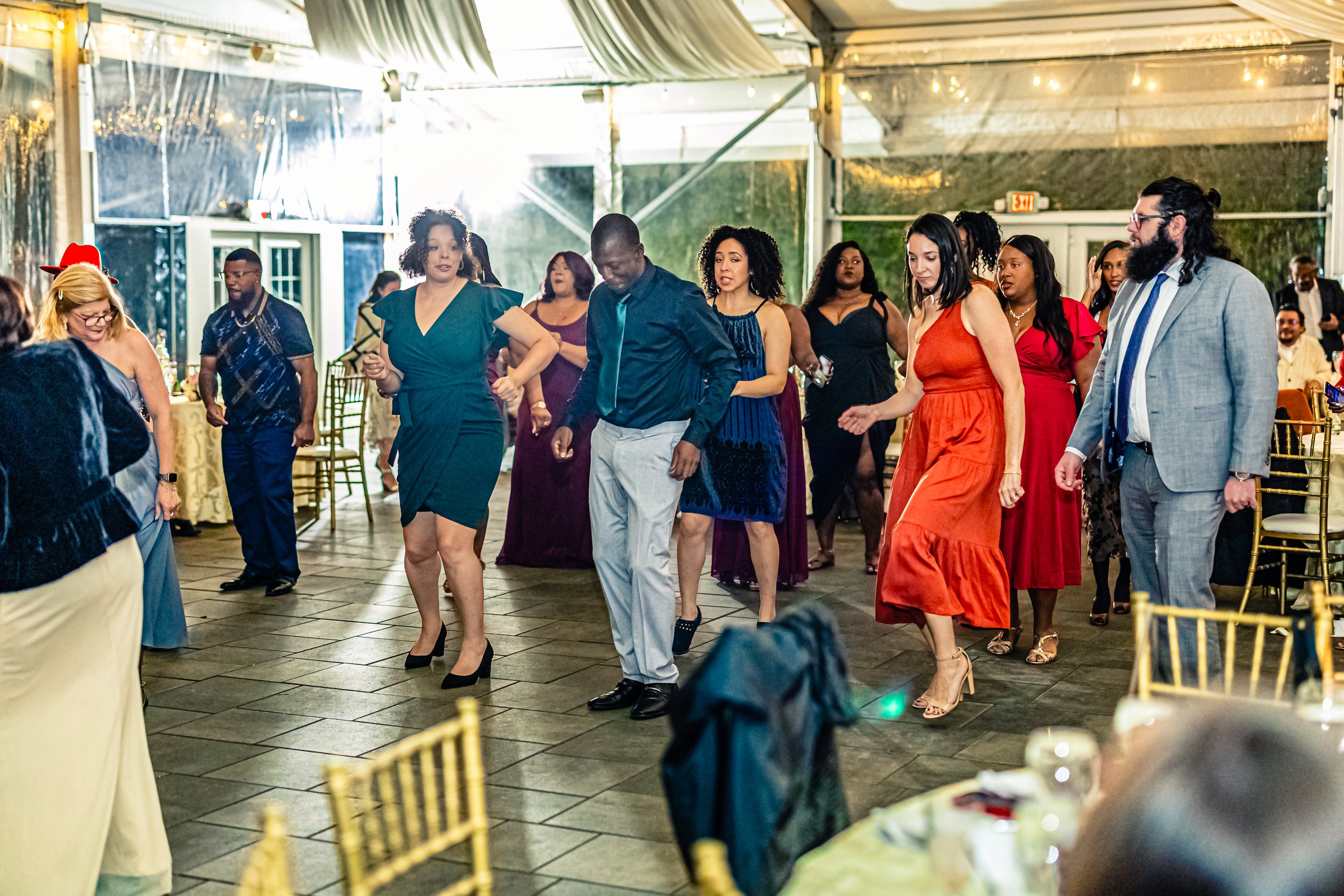 People dancing at a celebration or party in a decorated party tent with tables and gold chairs.