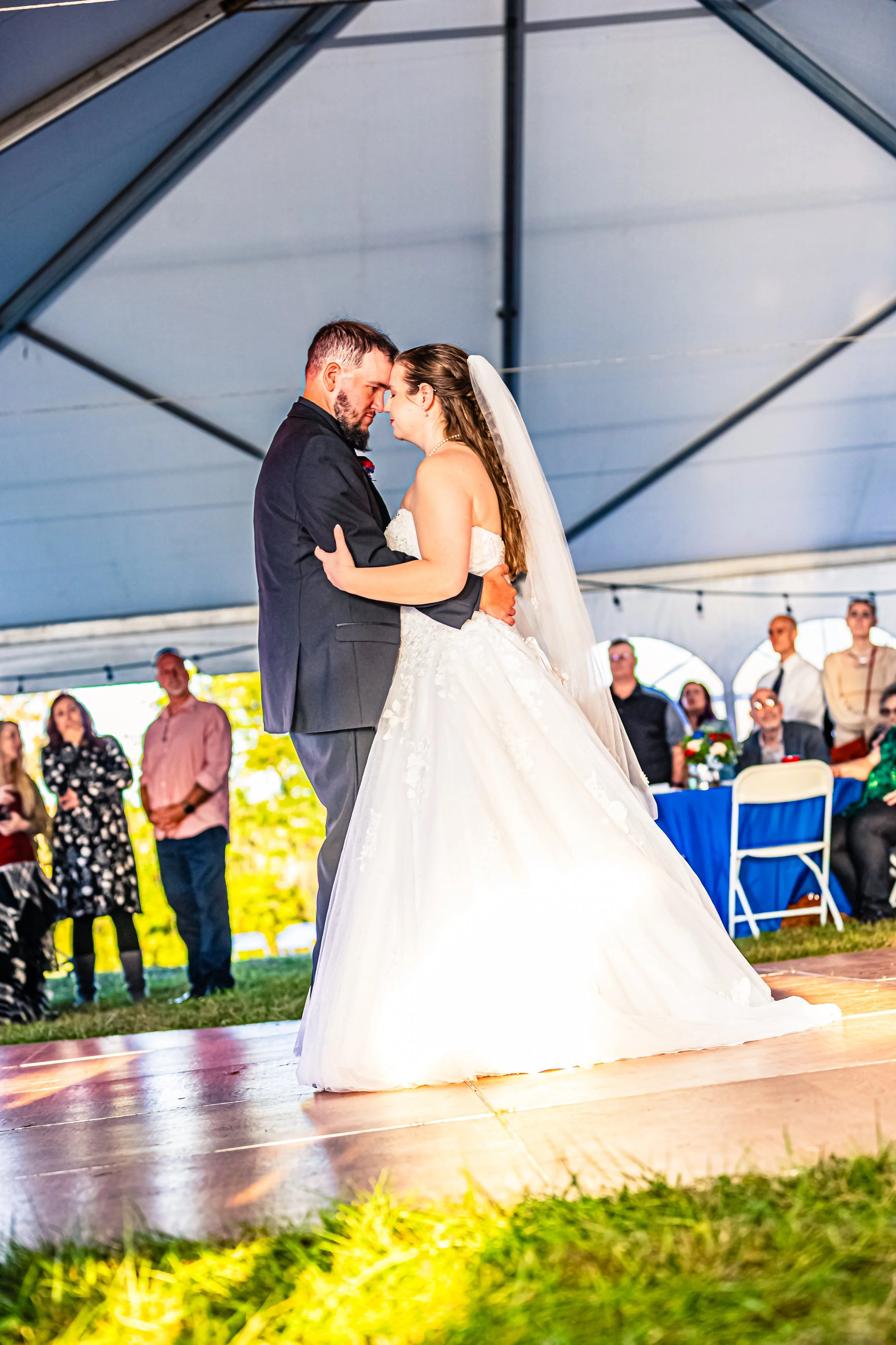 A bride and groom sharing their first dance at a wedding reception inside a large tent, with seated guests watching in the background.