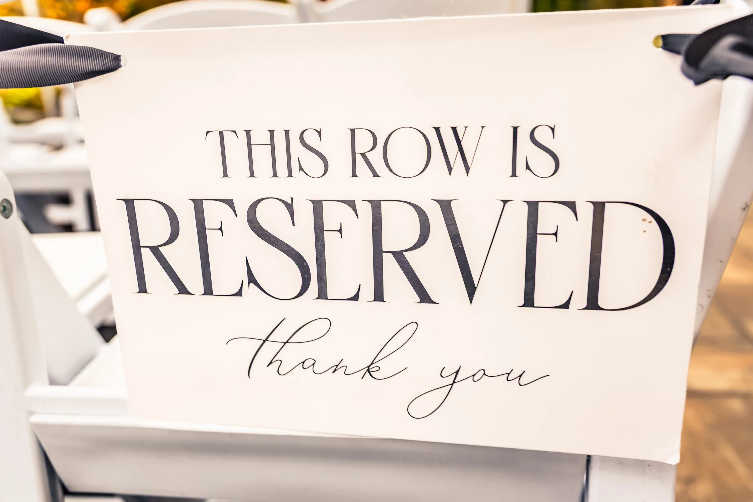A white sign with the text "This row is reserved, thank you" in black and cursive font.