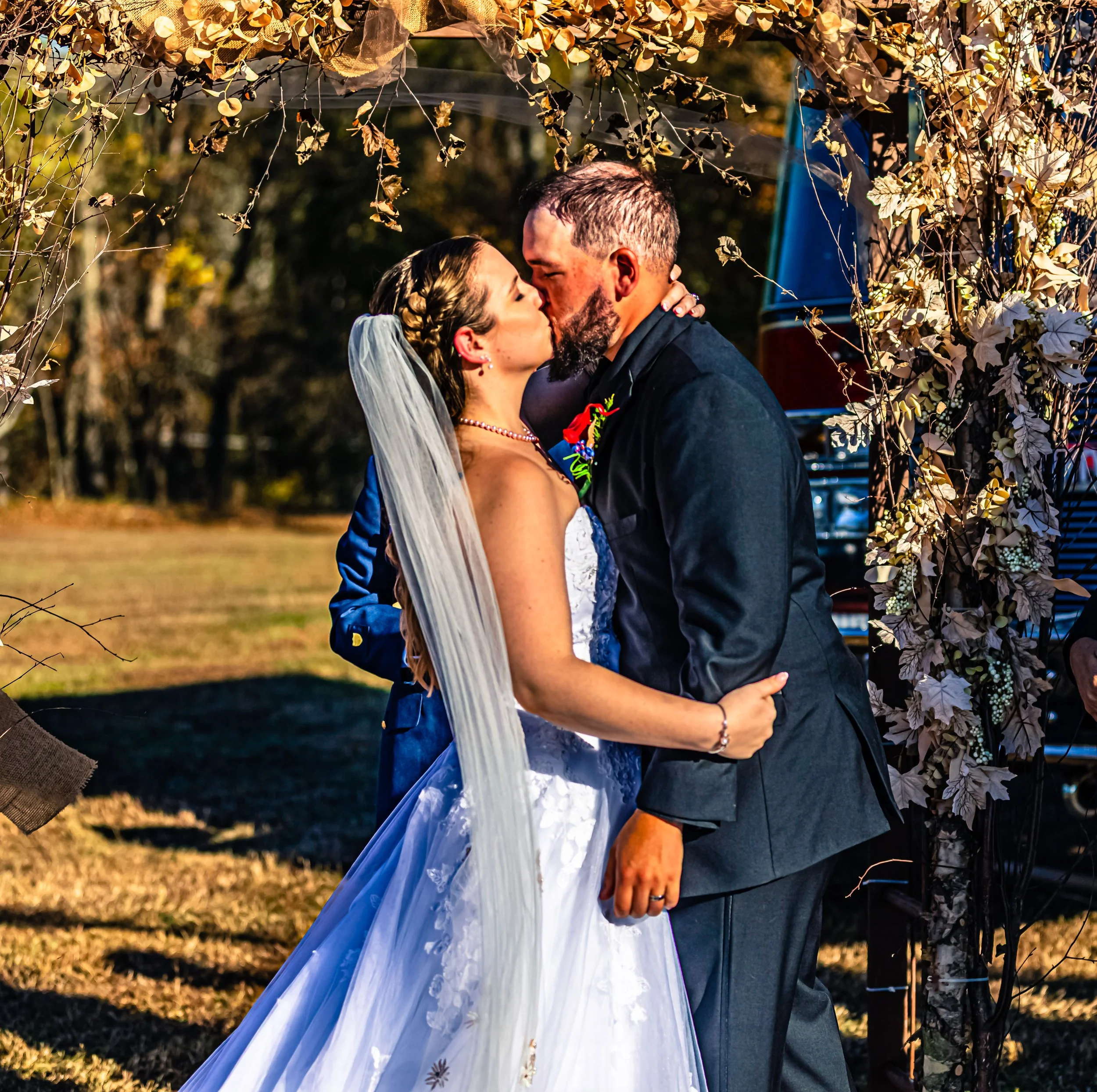 A bride and groom sharing a kiss at their outdoor wedding ceremony surrounded by a floral arch.