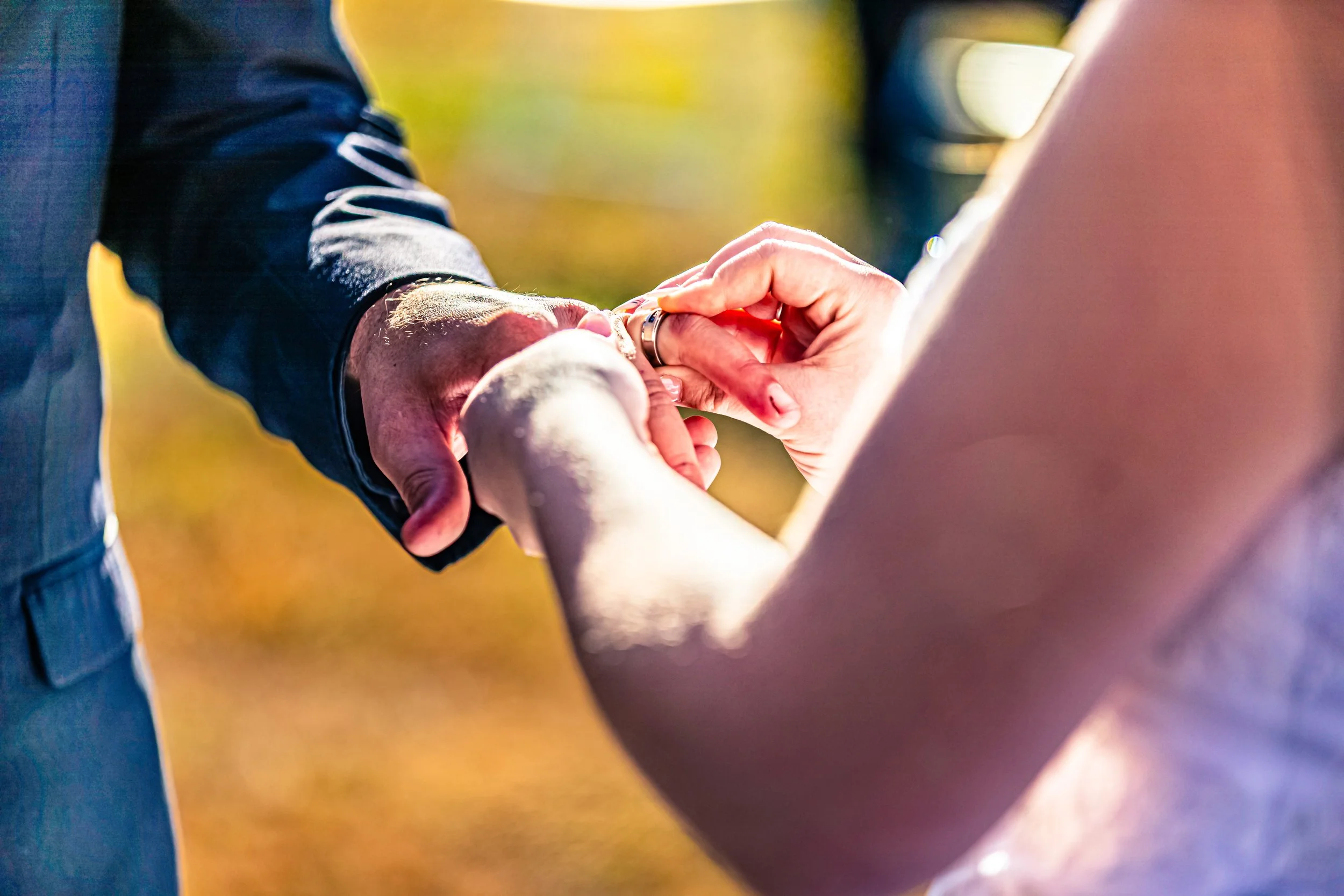 Close-up of a couple exchanging rings during a wedding ceremony outdoors, with a blurred natural background.