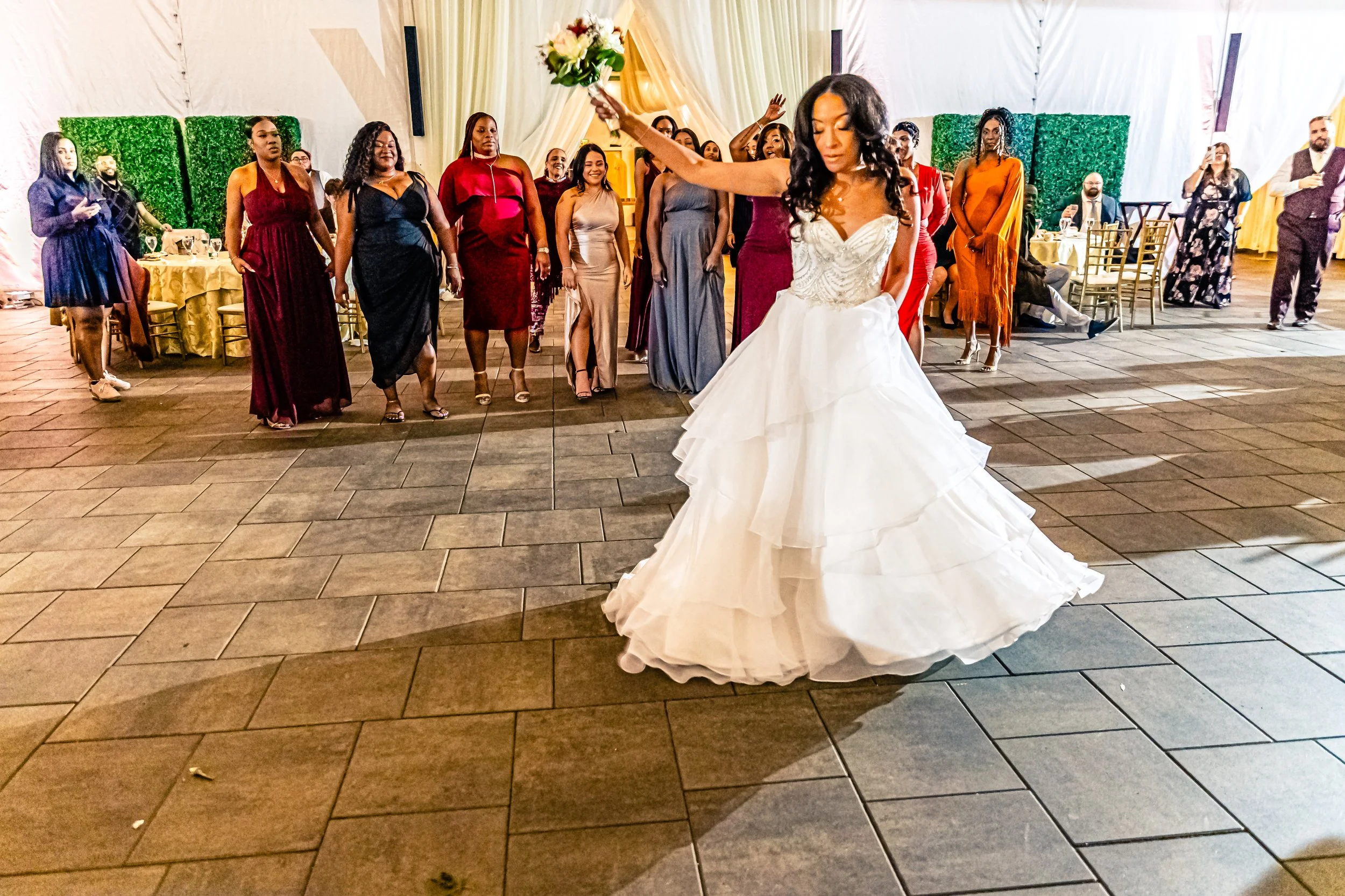 Bride in white wedding dress dancing at wedding reception with guests in the background.
