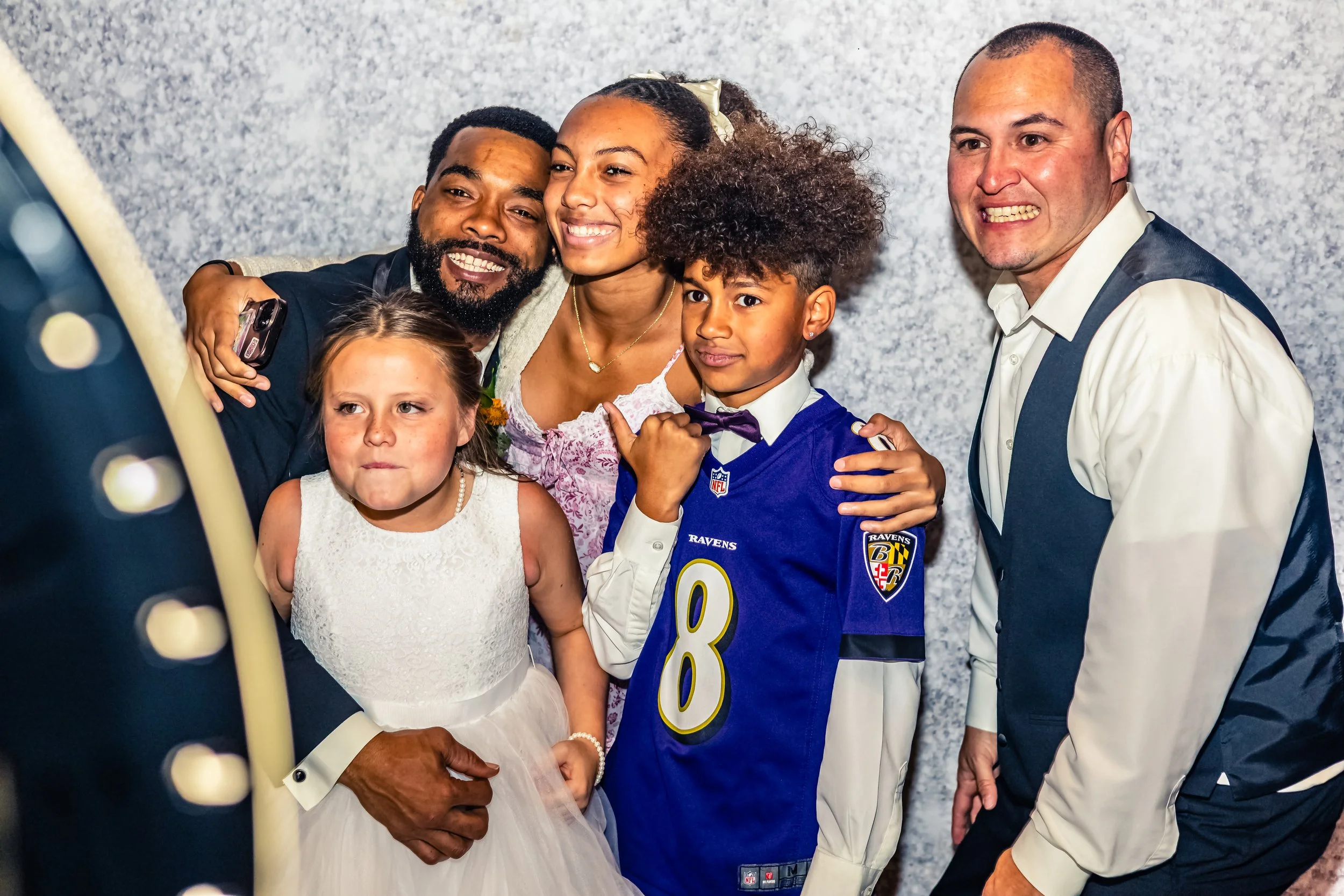 Group of six people, including two children and four adults, posing for a selfie in front of a grey textured background, celebrating a special occasion.