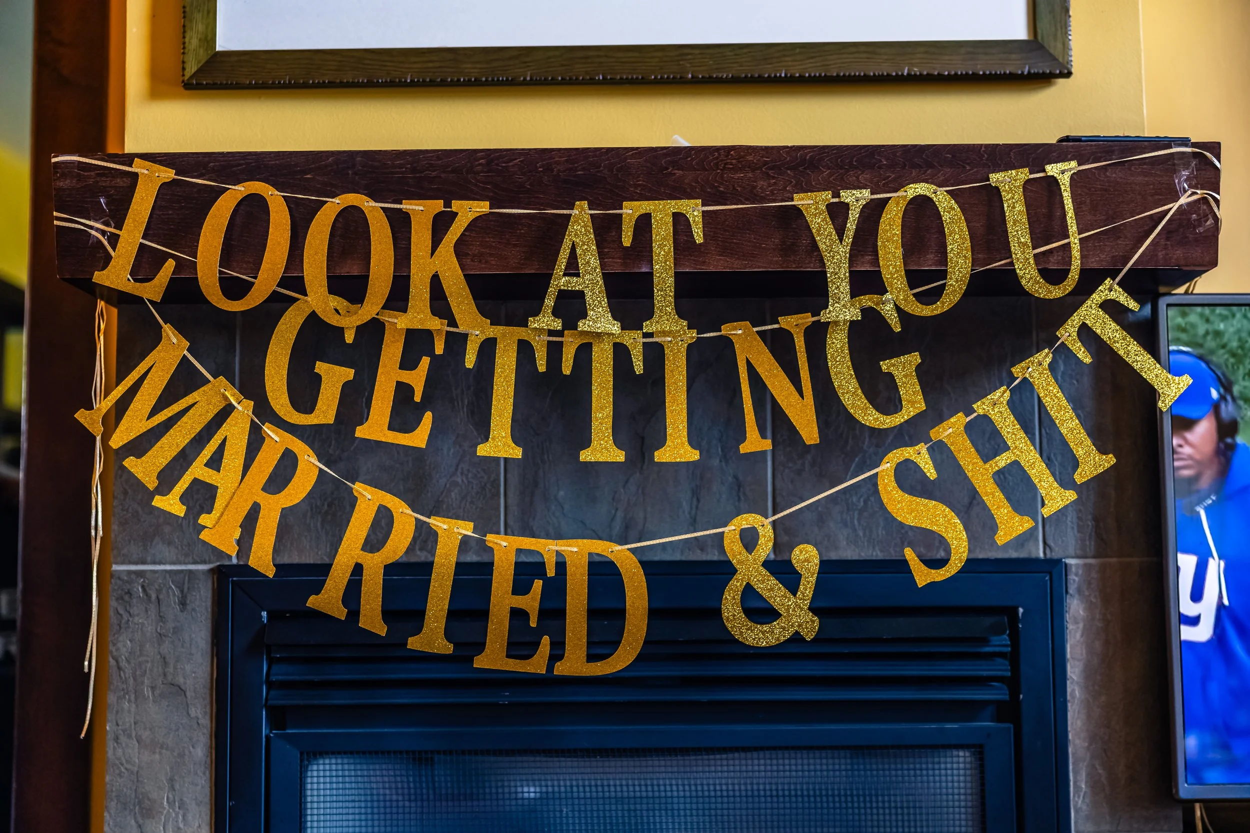 Gold glittery banner hung over a fireplace says 'Look at you getting married & stuff'.