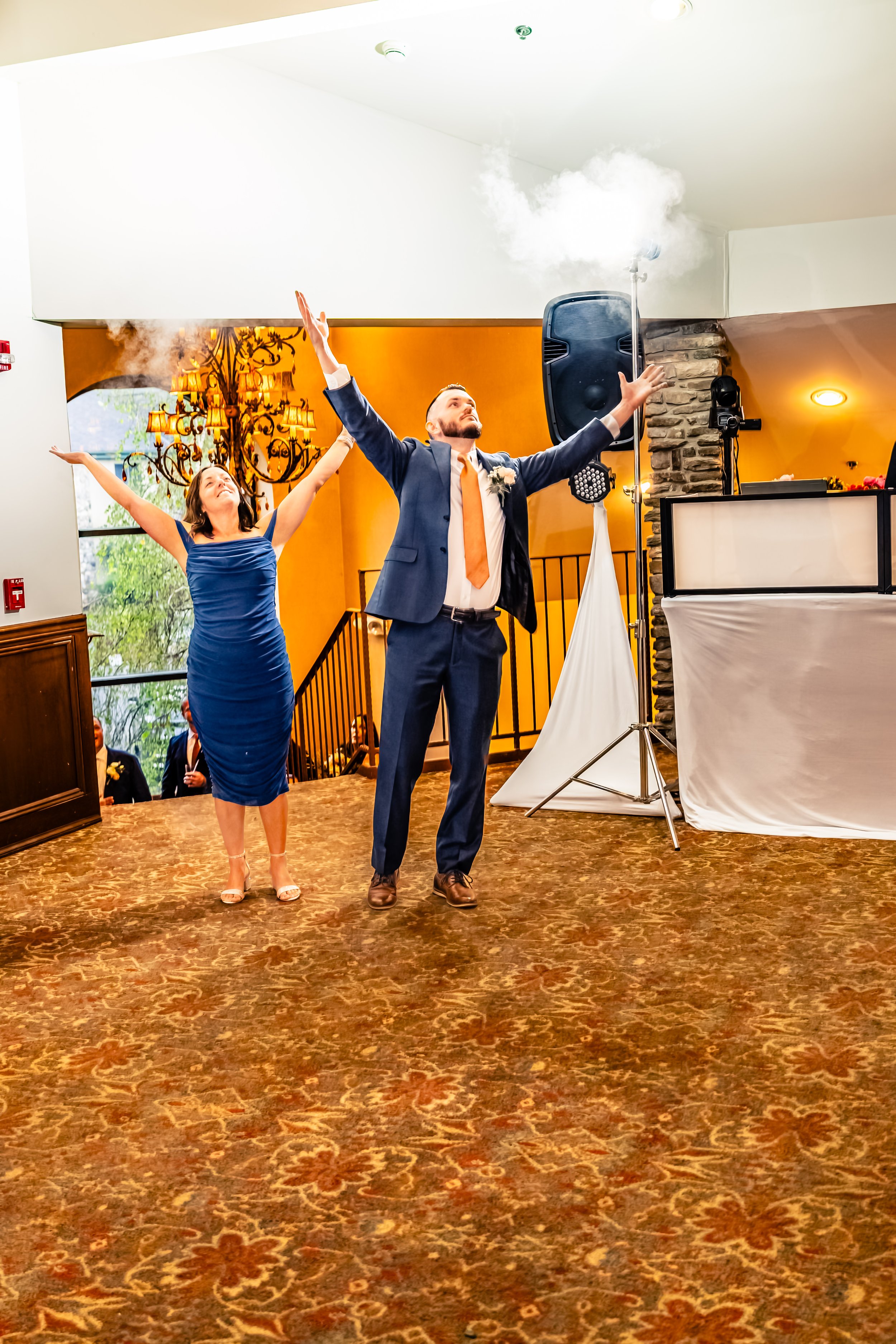 A bride and groom celebrating at a wedding reception with smoke effects, raising their arms joyfully.