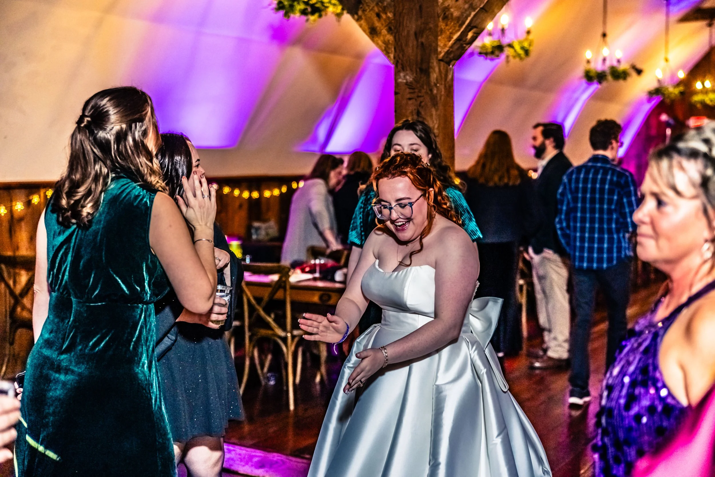 Group of people dancing and celebrating at wedding reception with festive lighting and decorations in a rustic venue.