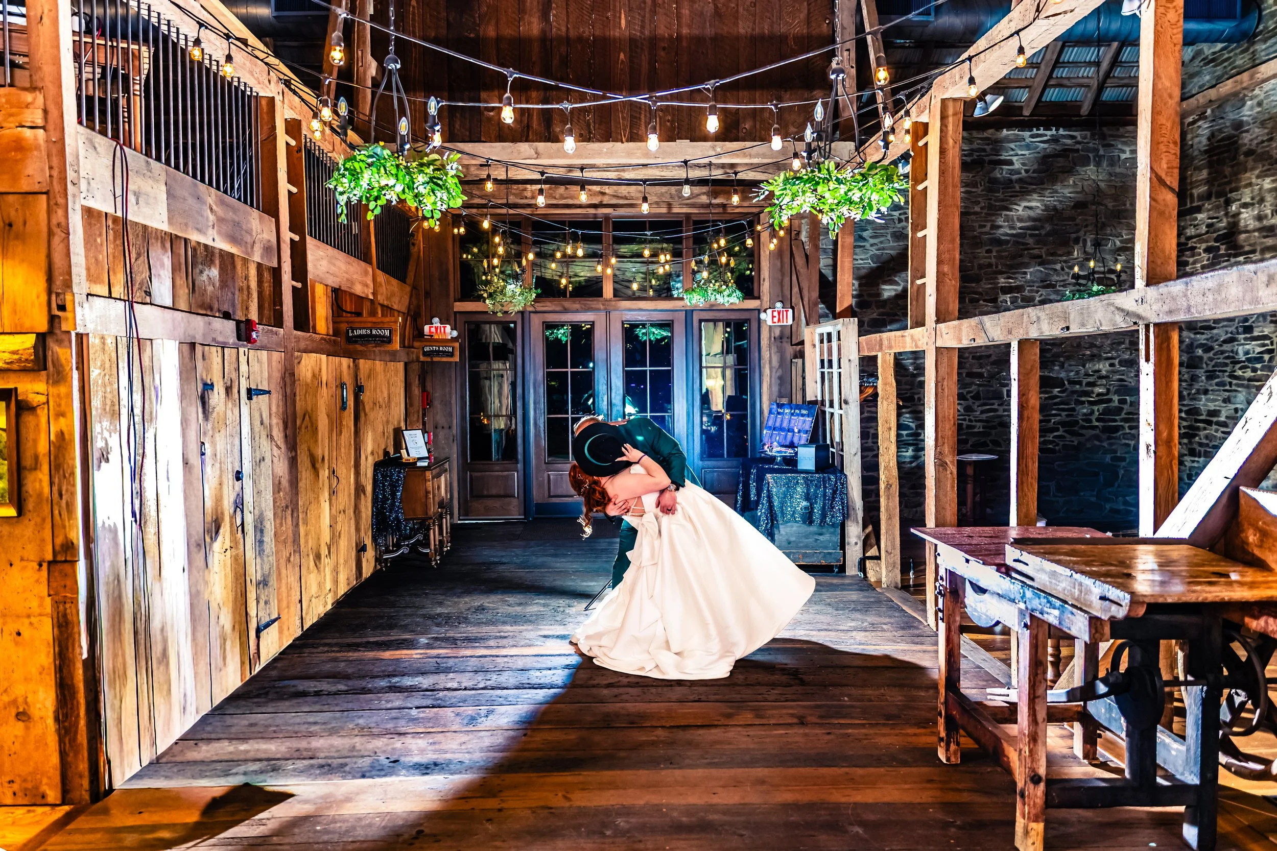 Couple sharing a dance at a rustic indoor wedding reception with string lights and greenery decor.