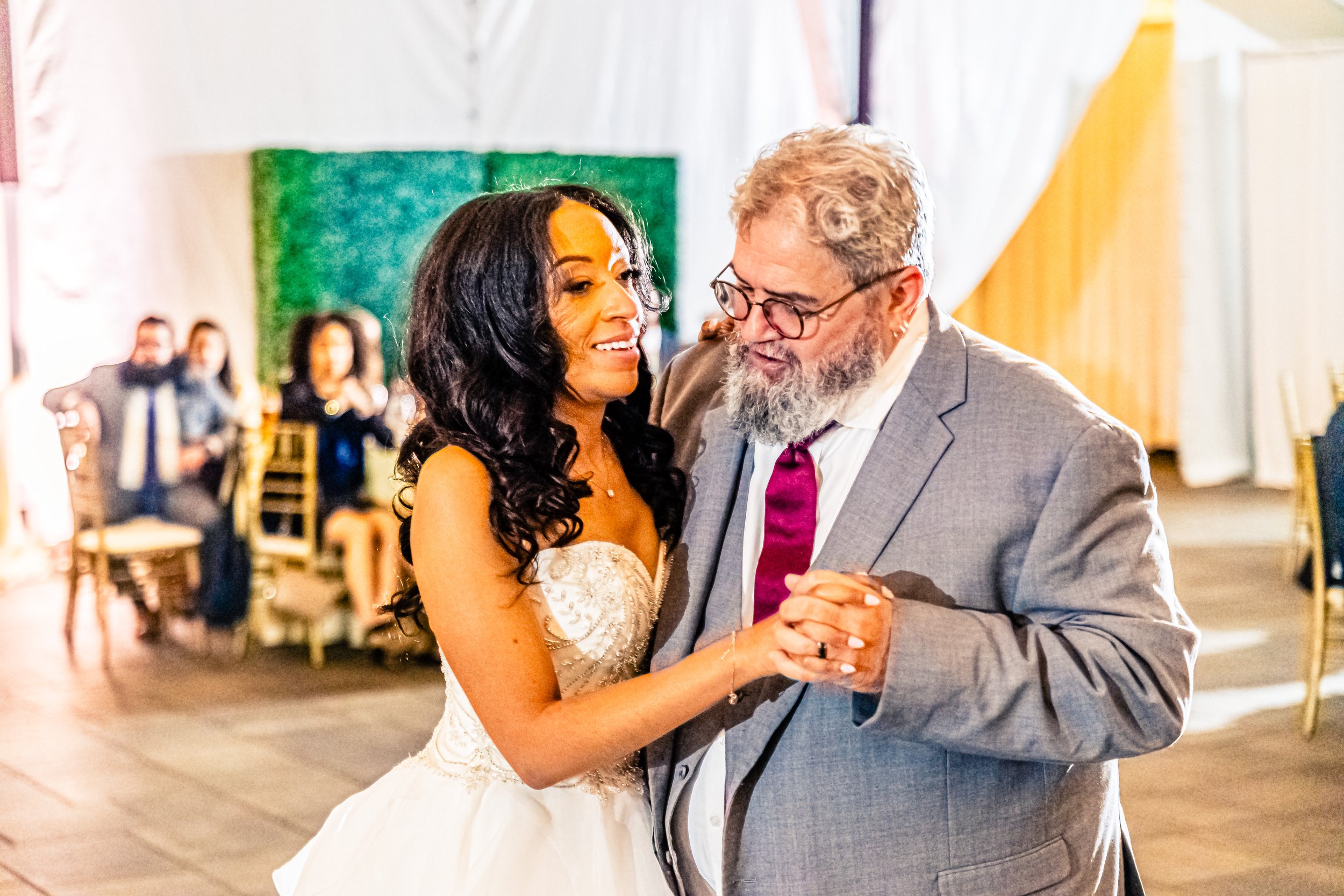 A woman in a wedding dress dancing with a man in a gray suit at a wedding reception.