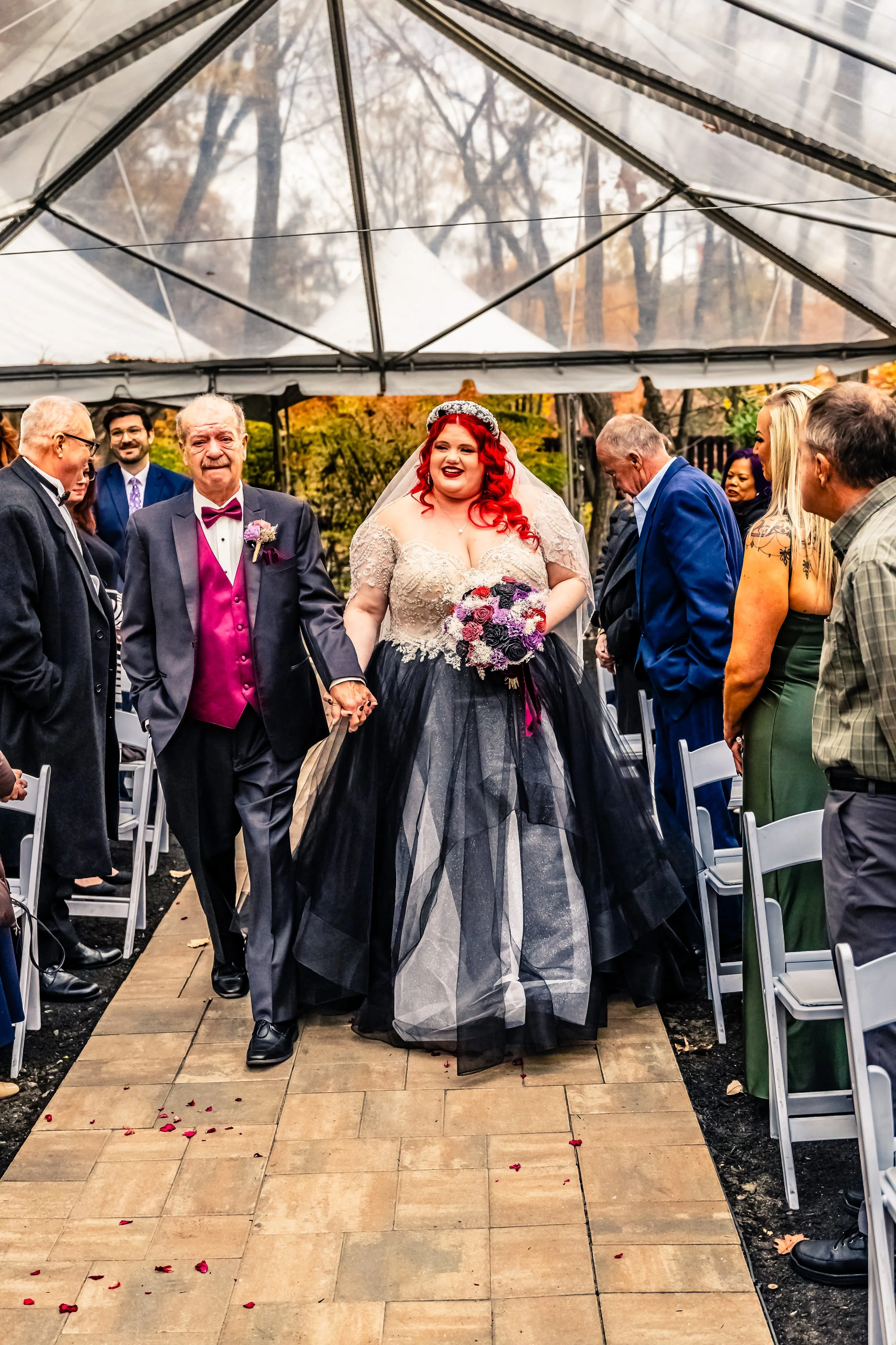 Bridal couple walking down the aisle under a clear tent, with guests on either side, during an outdoor wedding ceremony.