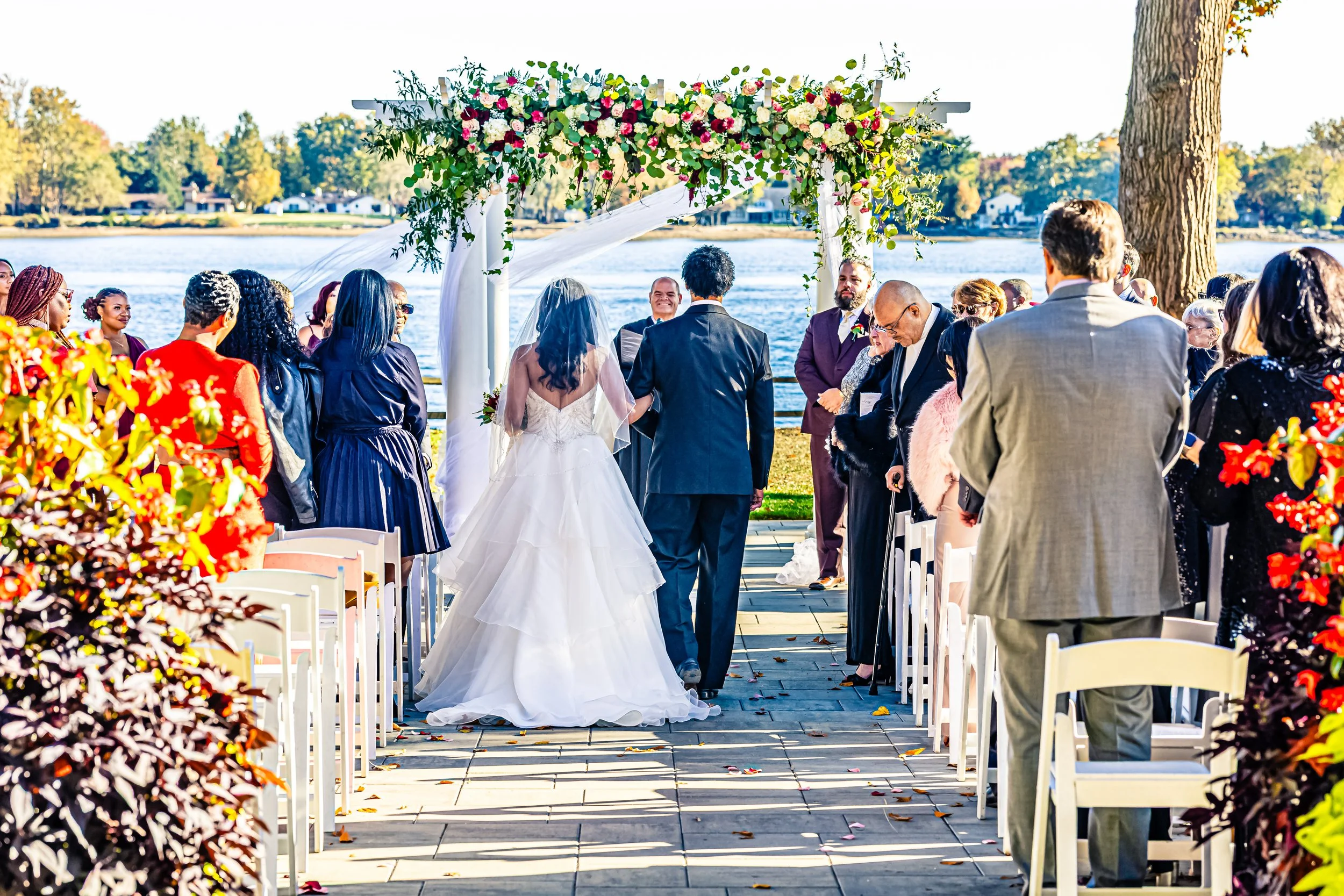 Bride and groom walking down aisle during outdoor wedding ceremony by a lake, surrounded by guests.