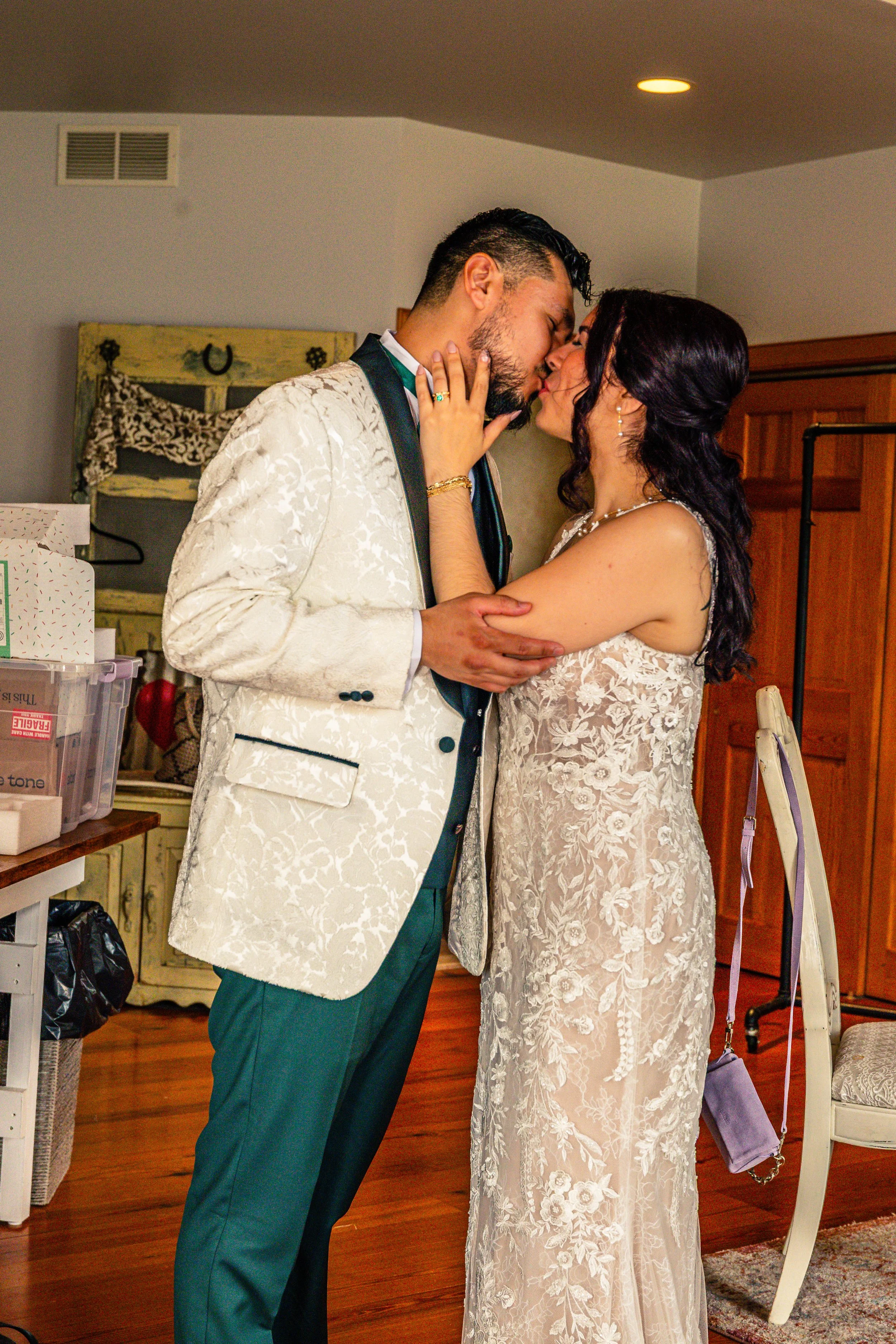 A couple dressed in wedding attire sharing a kiss indoors.