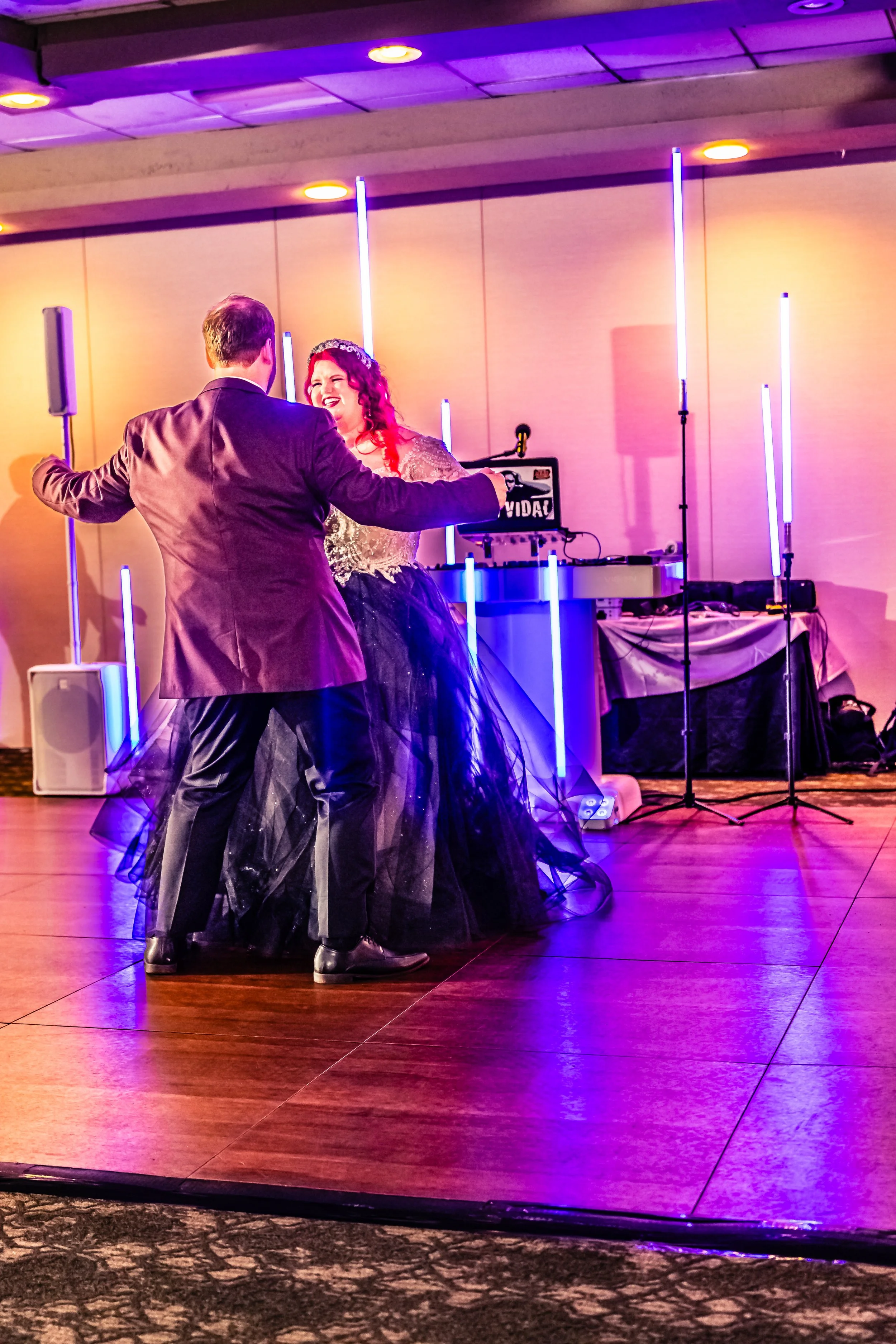 A man and woman dancing at a party with colorful neon lights and a DJ setup in the background.