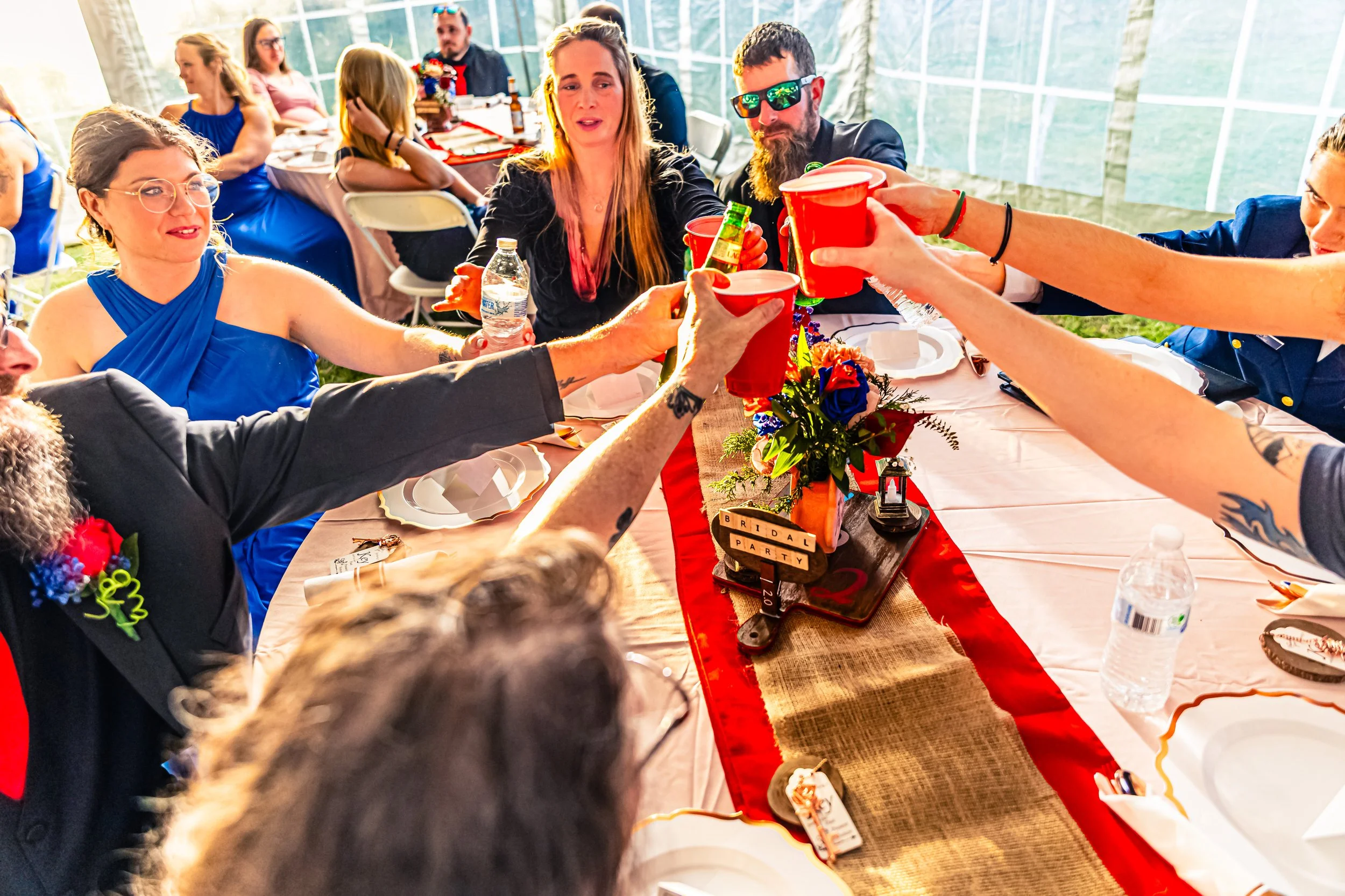 Guests at a wedding reception toasting with red cups at a decorated table with a 'Bridal Party' sign.