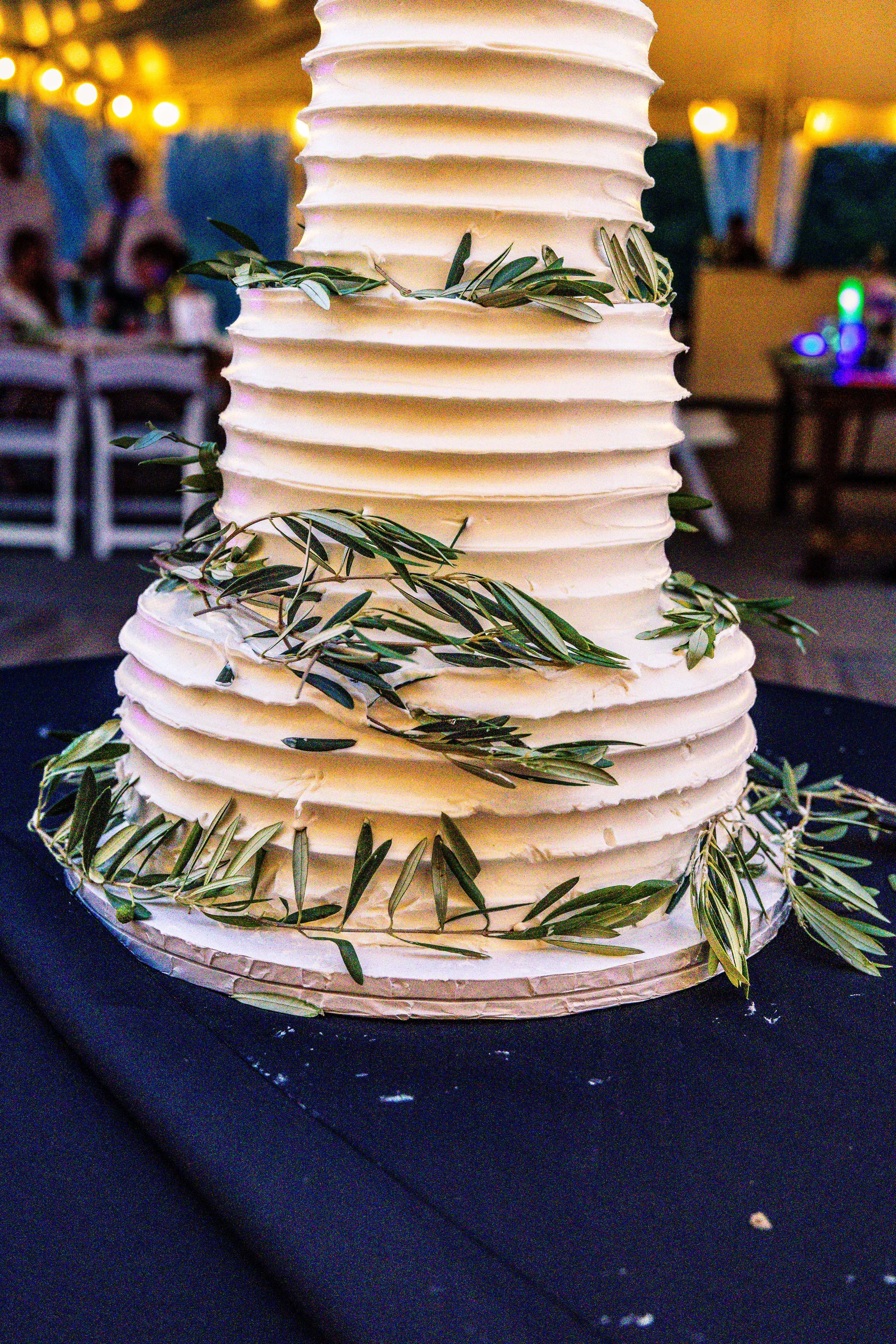 A tall, layered wedding cake with white frosting and green foliage decorations on a black table.