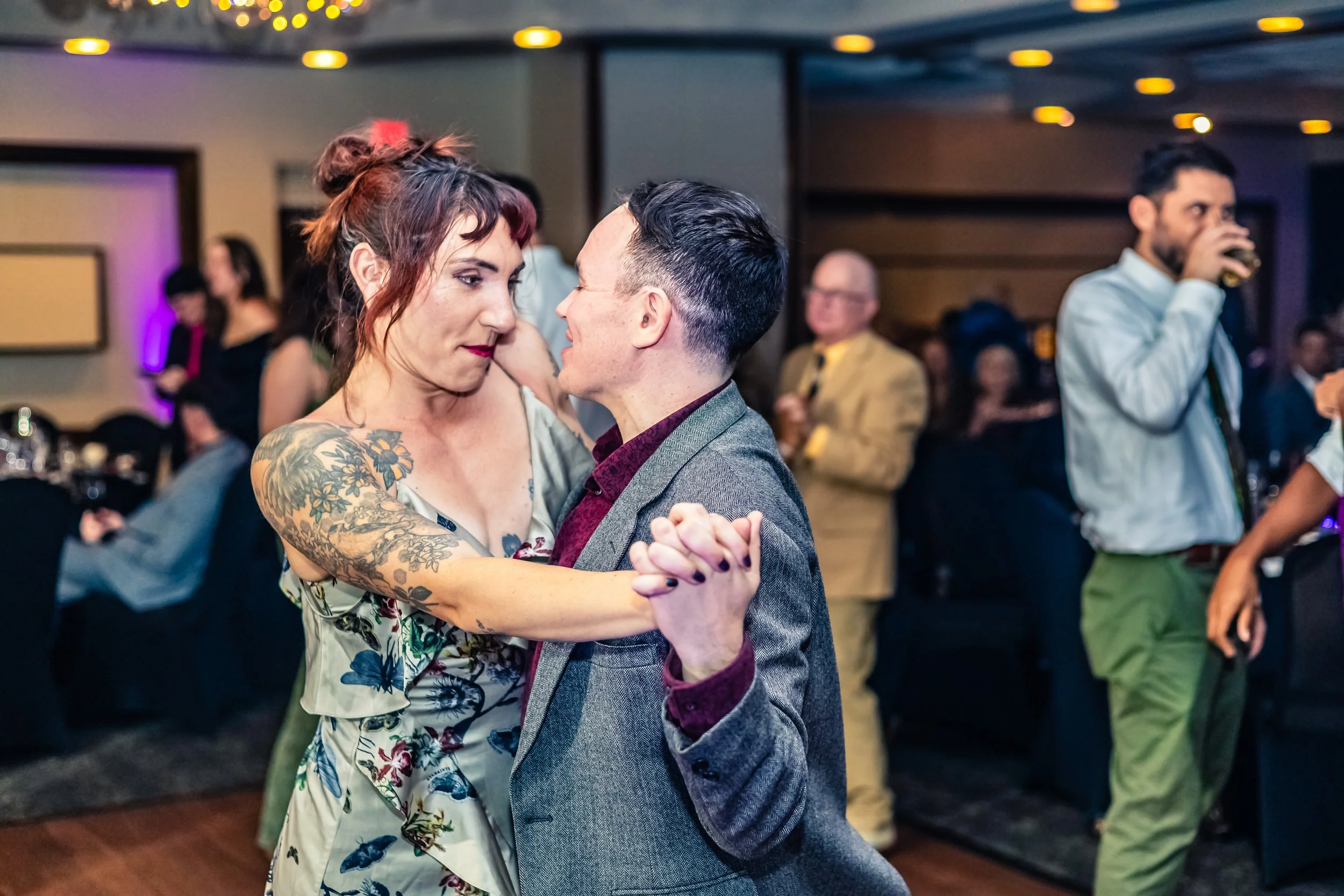 A man and woman are dancing closely at a party or wedding reception, with other people in the background enjoying the event.